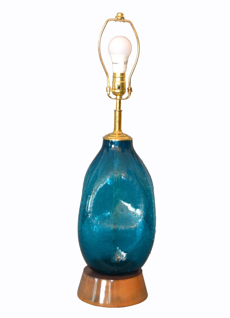 Mid-Century Modern blue hand blown art glass table lamp.
The lamp has a wooden base, brass details and comes with Harp and Finial.
It is in perfect working condition and uses a max. 60 watts light bulb.
Note: Shade is not included.