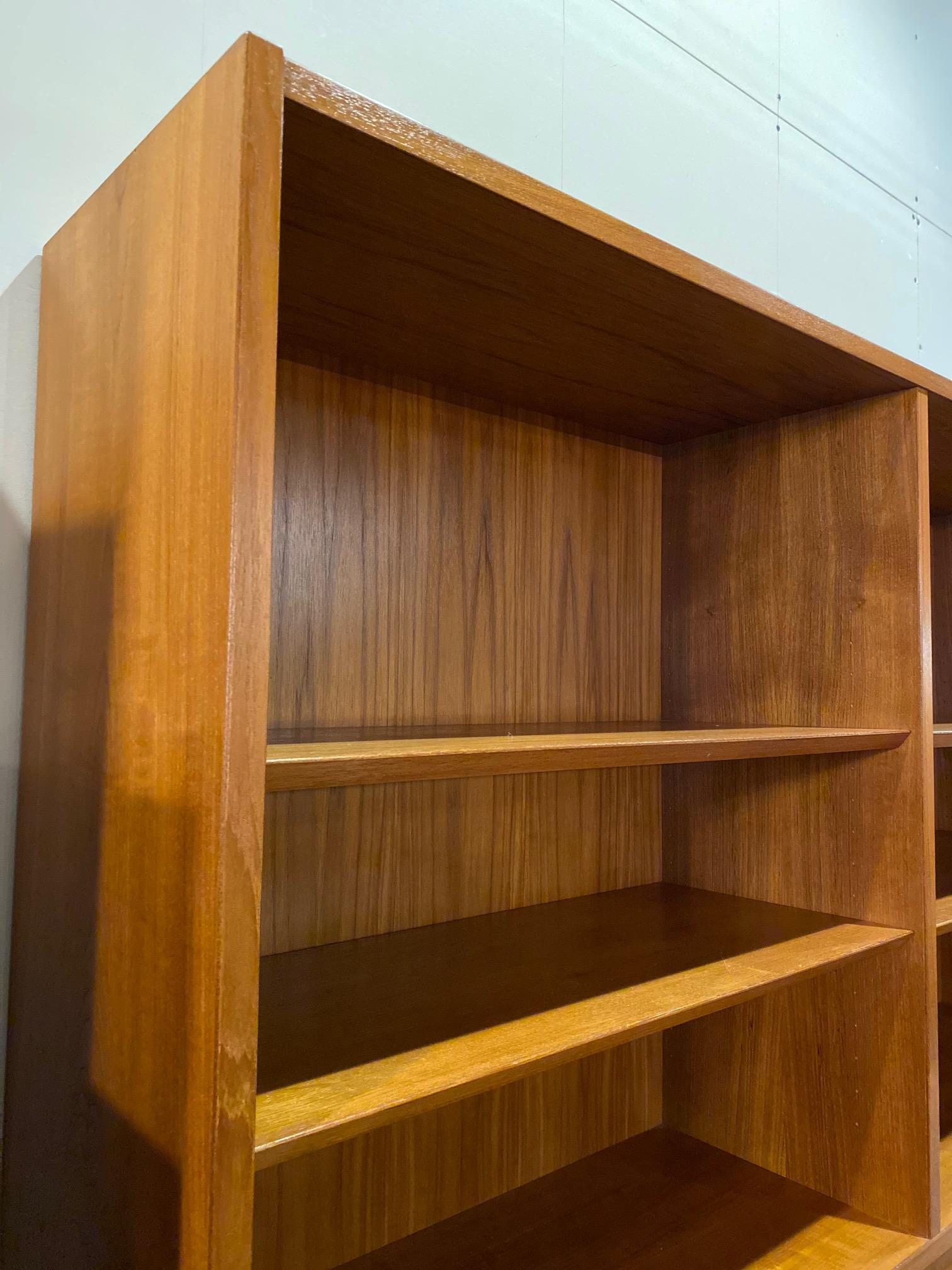 Mid-century Danish bookcase in teak by Carlo Jensen for Hundevad features a bookcase with drop desk. This bookcase comes in two pieces, shelving on top and drop down desk with sliding doors on bottom that include pull out trays. Bottom tray is lined