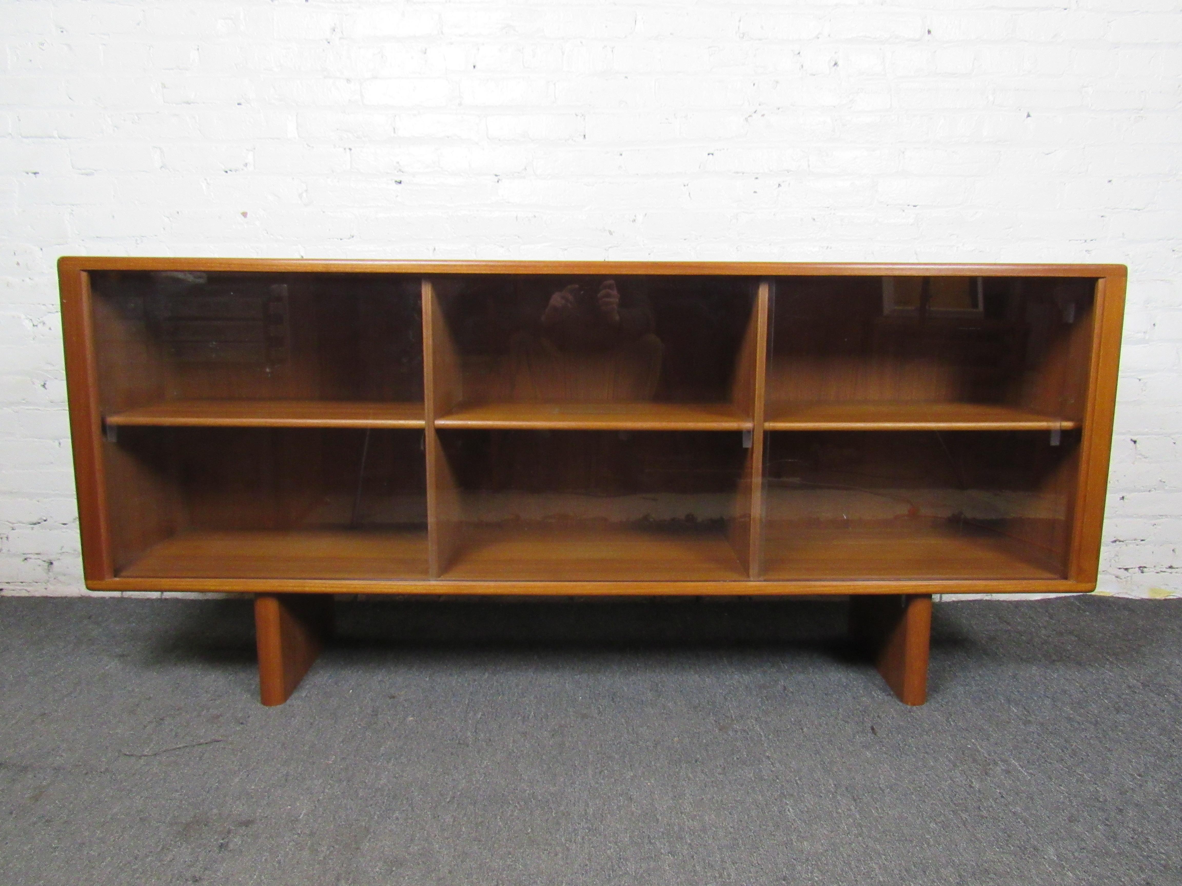 This vintage teak bookcase features a unique design that allows it to be used as a console. Sliding glass doors accent a rich teak woodgrain and Mid-Century Modern design. Please confirm item location with seller (NY/NJ).