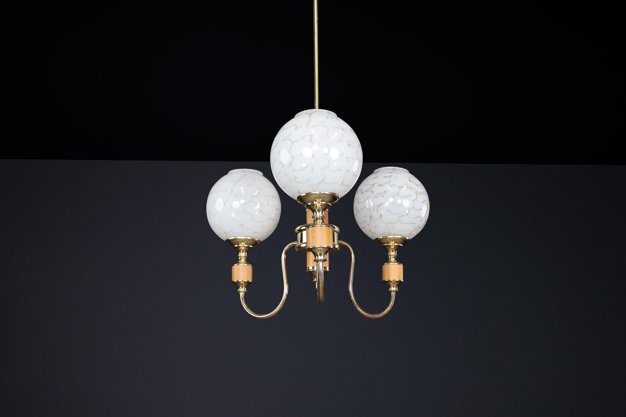 This elegant mid-century modern chandelier, produced in Czechoslovakia during the 1970s, embodies the era's signature blend of sculptural form and functional elegance. The fixture features three gracefully curved brass arms radiating from a central