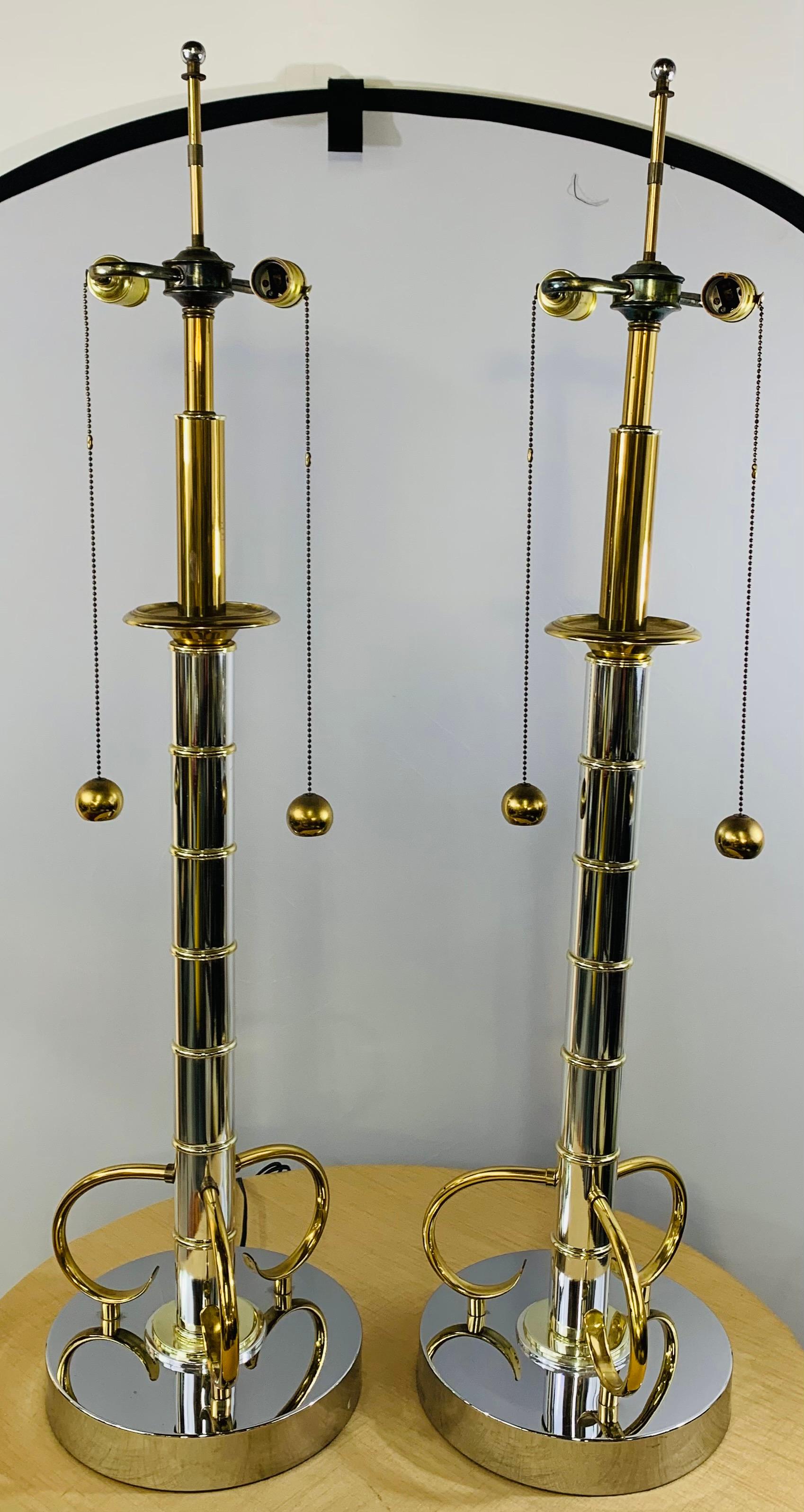 An elegant pair of Mid-Century Modern brass and chrome table lamps in the style of Tommi Parzinger. Made in faux bamboo style with alternating nicely polished brass and chrome bands, the tables lamps stand on a scroll three legs standing on a round