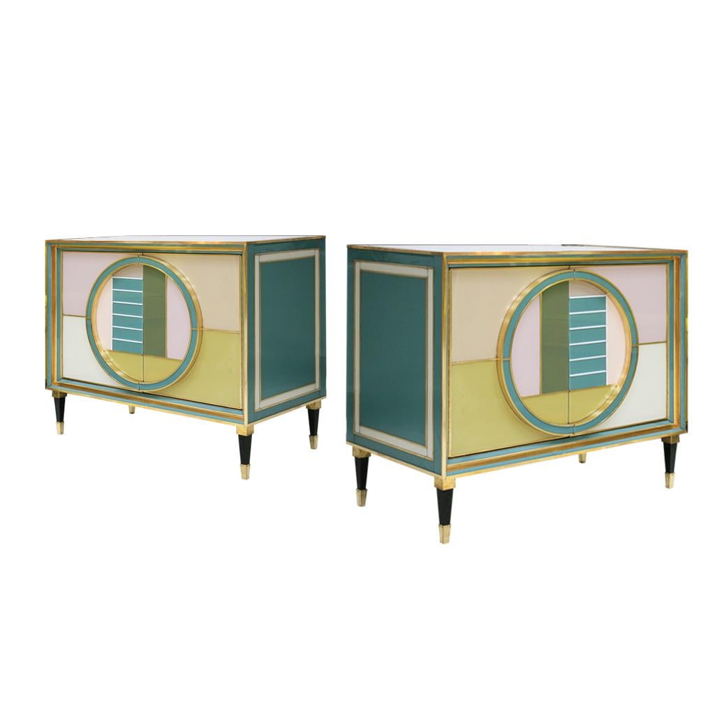 Pair of Italian sideboards composed of two folding doors and interior covered in grey velvet with a shelve. Made of solid wood structure covered in colored glass and brass details. White glass and brass conical shape legs.

Production can last