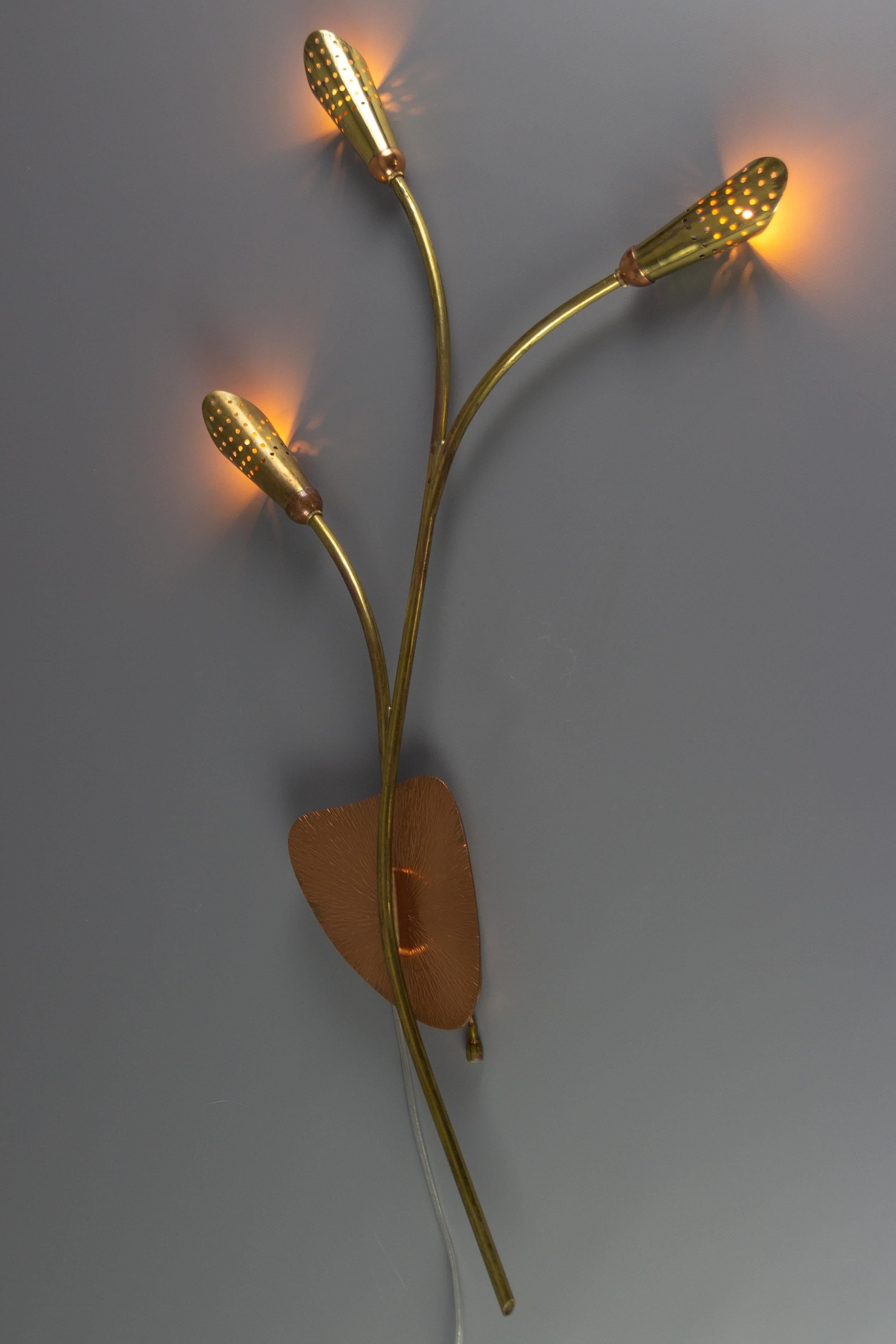 A charming Mid-Century Modern brass and copper sconce, Germany, 1970s. This beautiful wall lamp has three perforated cone-shaped shades that create a romantic diffusion of light. A real eye-catcher is a decorative base with a sunburst-like