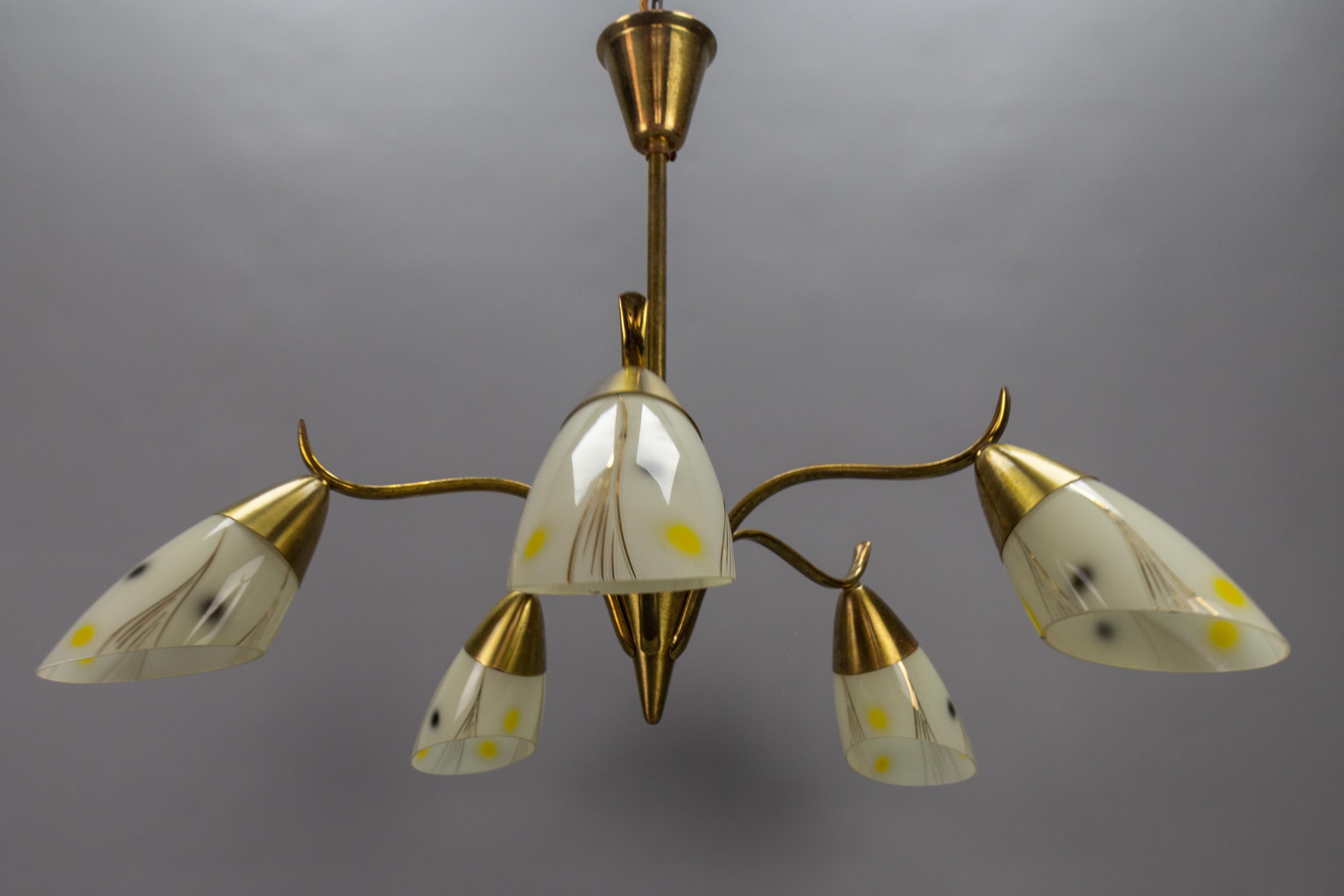 Mid-Century Modern brass and glass five-light Sputnik chandelier, Germany, circa the 1950s.
This adorable vintage Rockabilly chandelier features a brass and metal frame with five arms, each with an ivory-colored glass bag-shaped lampshade, adorned