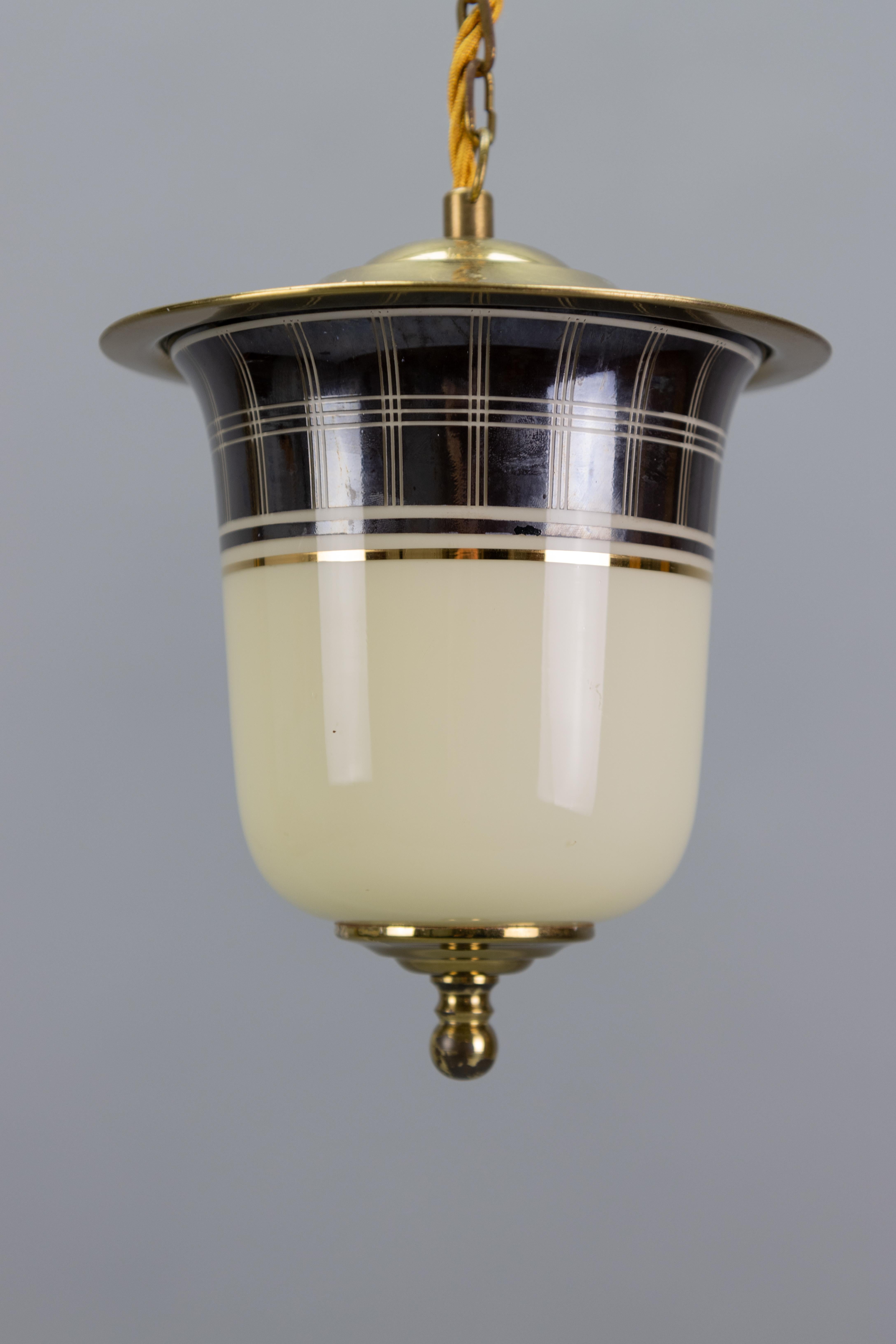 Una raffinata lampada a sospensione della Germania del Mid-Century Modern, risalente agli anni '50 circa, con un caratteristico paralume in vetro a forma di lanterna. 
La parte superiore è decorata con una fascia dipinta e un delicato rivestimento