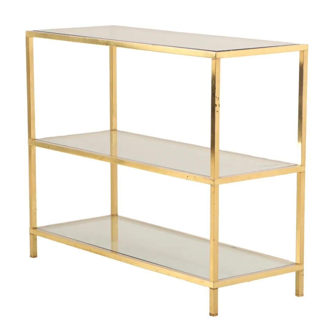 This vintage brass and glass three-tier etagère, circa 1970, showcases a sleek, minimalist design with a straight, square frame that exudes a timeless, modern sophistication. The frame, made of polished brass, offers a gleaming contrast to the