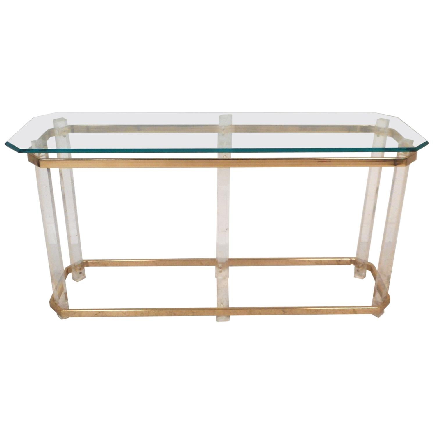 This beautiful vintage modern console table features a Lucite and brass frame with a glass top. An impressive design held together with six Lucite pillars and two flat bar brass wrap-around supports. A thick glass top with bevelled edges and a light