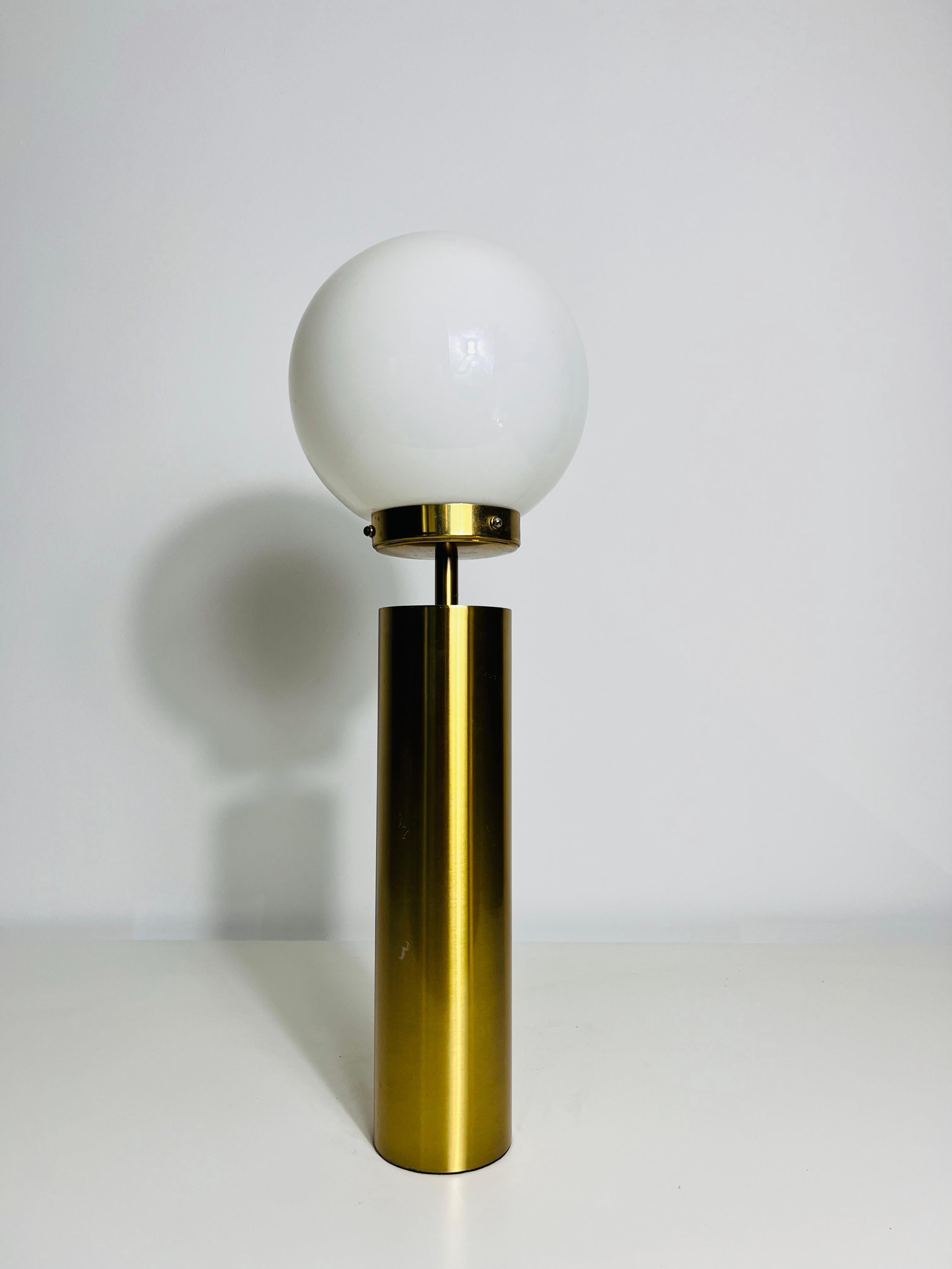 Esta distintiva lámpara de sobremesa de la Alemania de los años 60 muestra un diseño moderno de mediados de siglo con una clara influencia de la Bauhaus. La lámpara tiene una elegante base cilíndrica de latón que soporta un delgado tallo, que