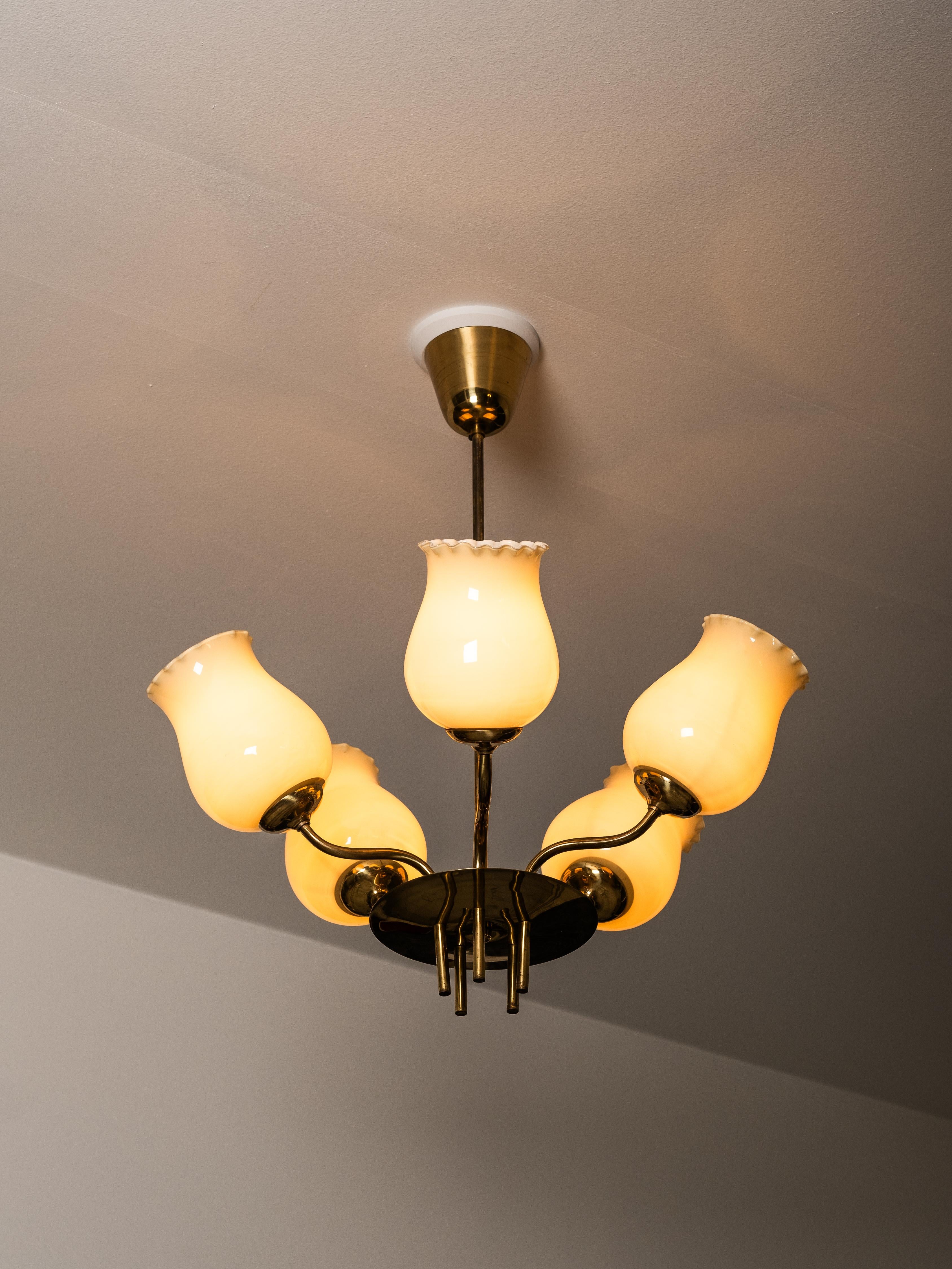 Raffinato lampadario di metà secolo in ottone e vetro opalino di Itsu (Itsu-Suomen Sähkö), Finlandia, anni Cinquanta. Il lampadario è caratterizzato da cinque paralumi a tulipano in vetro opalino dolcemente incurvati e sostenuti da bracci in ottone