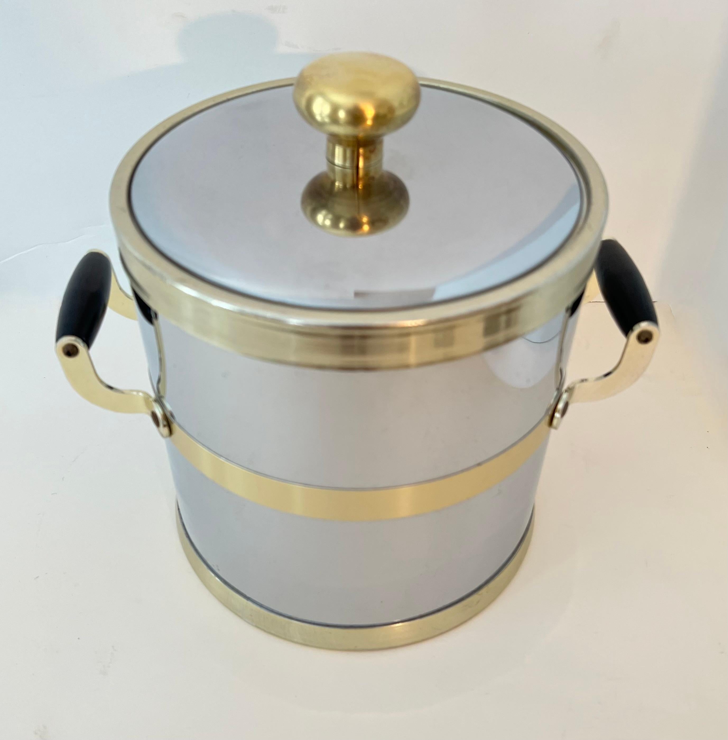 A sleek and stylish Mid-Century Modern ice bucket in polished chrome with brass detailing and black wooden handles. The piece has a plastic liner, all in great condition. 

A compliment to any bar.