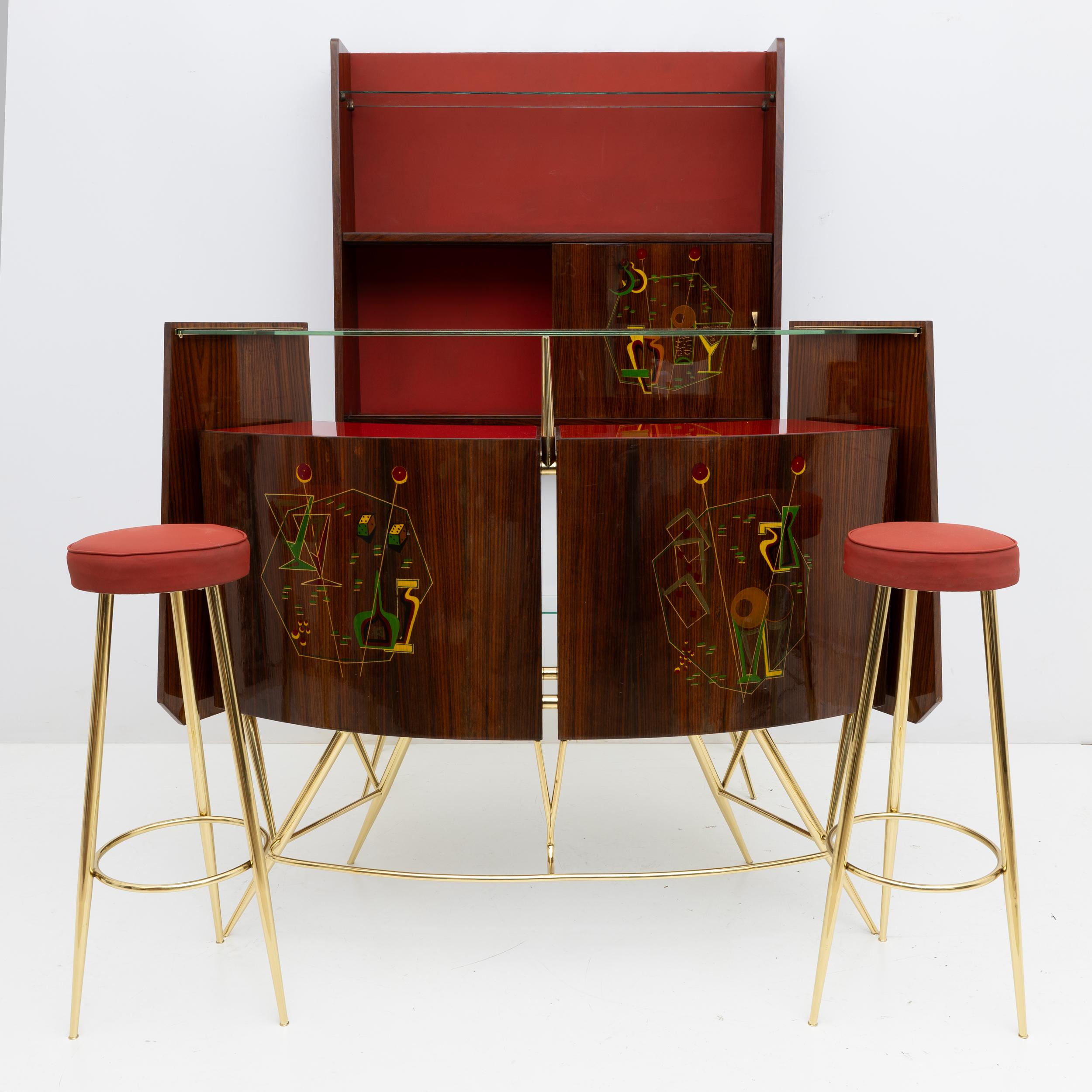 Mobile bar in ottone e noce con 2 sgabelli, Italia, anni '50. Set composto da due sgabelli in ottone e skai, bancone e mensola in legno, ottone e vetro; l'ottone è stato lucidato, così come le parti in legno, il rivestimento in tela rossa è