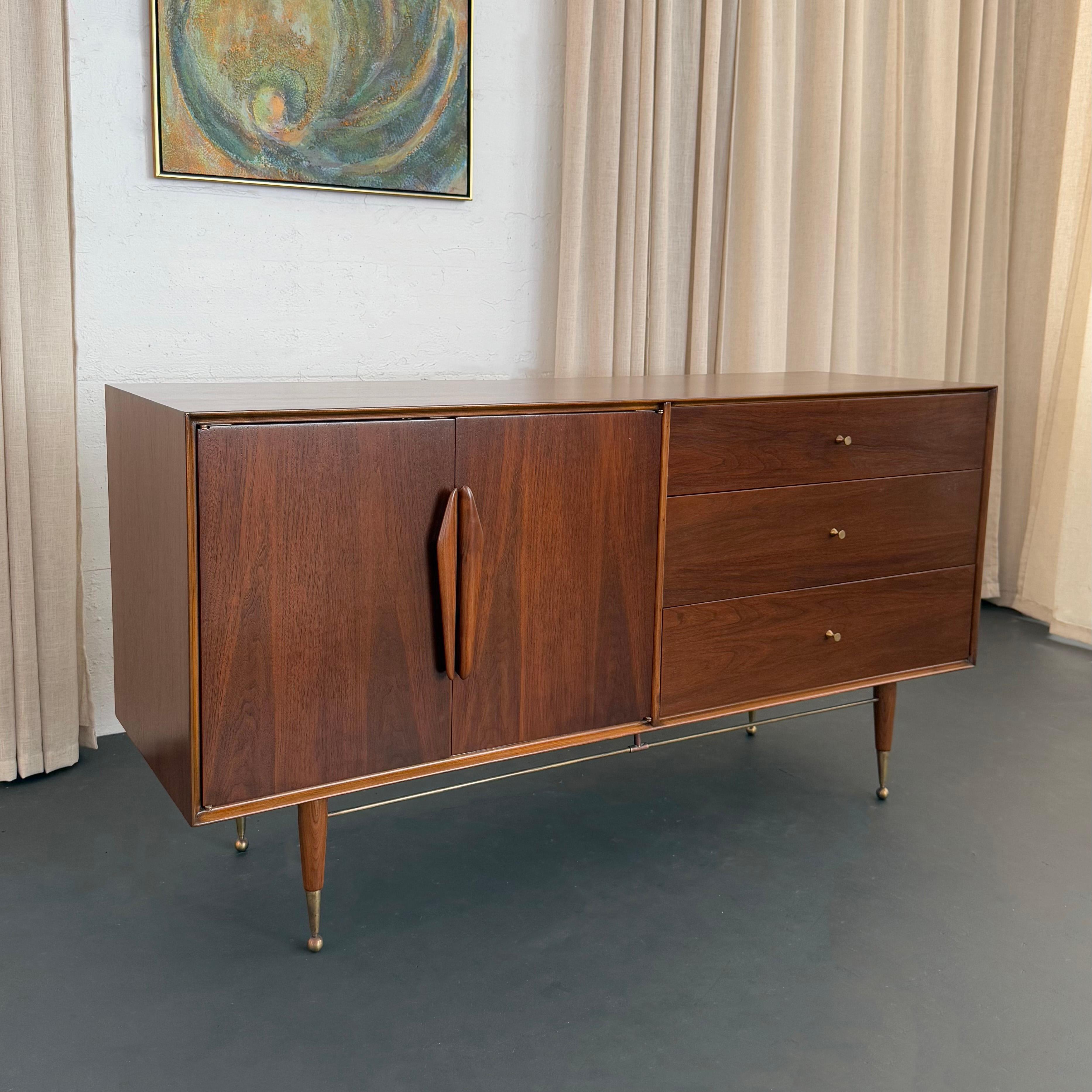 Este impresionante aparador de nogal y latón se atribuye a Kent Coffey, hacia la década de 1950. Este aparador es la personificación del diseño moderno de mediados de siglo, con sus líneas limpias y acentos atómicos. El mueble presenta un cálido