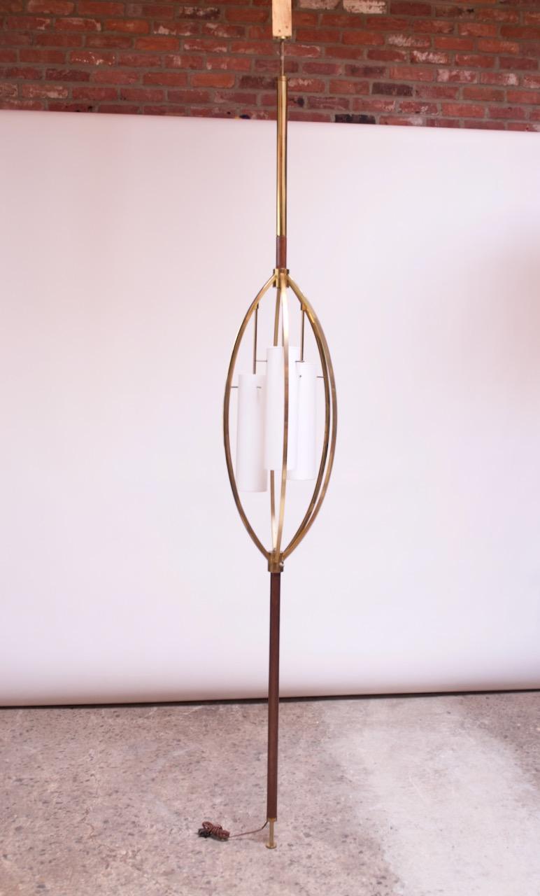 American Modern tension lamp composed of a brass and walnut veneer pole supporting a tubular brass ellipse carriage, which houses three, cylindrical white cased-glass fixtures, circa 1950s. Easily transportable and simple to assemble / disassemble: