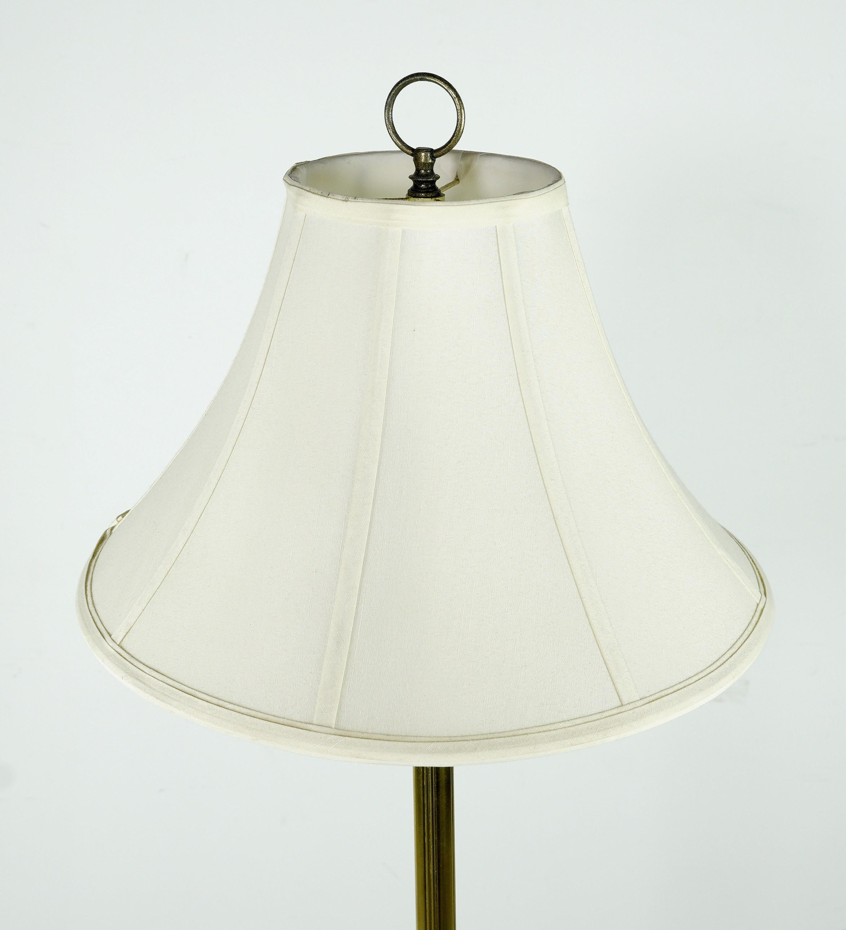 Mid-Century Modern style floor lamp having an antique brass finish. Features a center glass circular glass tabletop and the original white shade. Takes one standard medium base light bulb. Cleaned and restored. Original patina on the antique brass