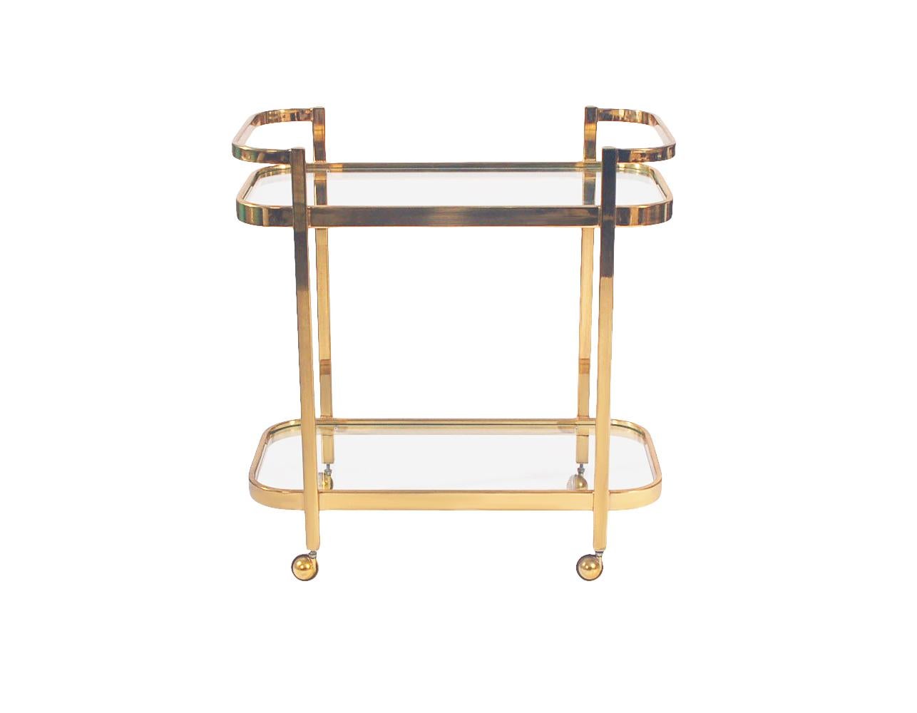 A simple, modern and elegant bar cart circa 1970's. It features brass framing with clear glass shelving.