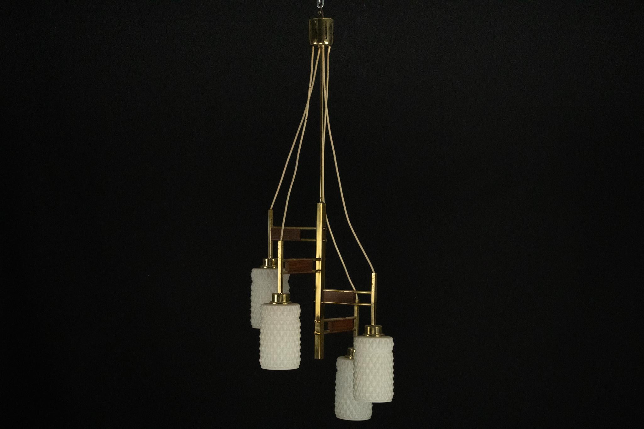 Questo lampadario di grande effetto sfoggia un classico design moderno di metà secolo, combinando eleganti dettagli in ottone con caldi accenti in legno. Realizzato in Italia, presenta quattro paralumi in vetro bianco testurizzato disposti intorno a