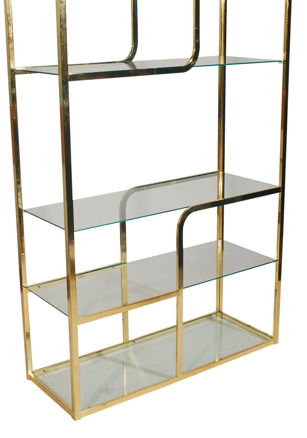 A contemporary brass étagère from the 1970s in the style of Milo Baughman. It features an asymmetrical brass frame design with clear glass shelving.