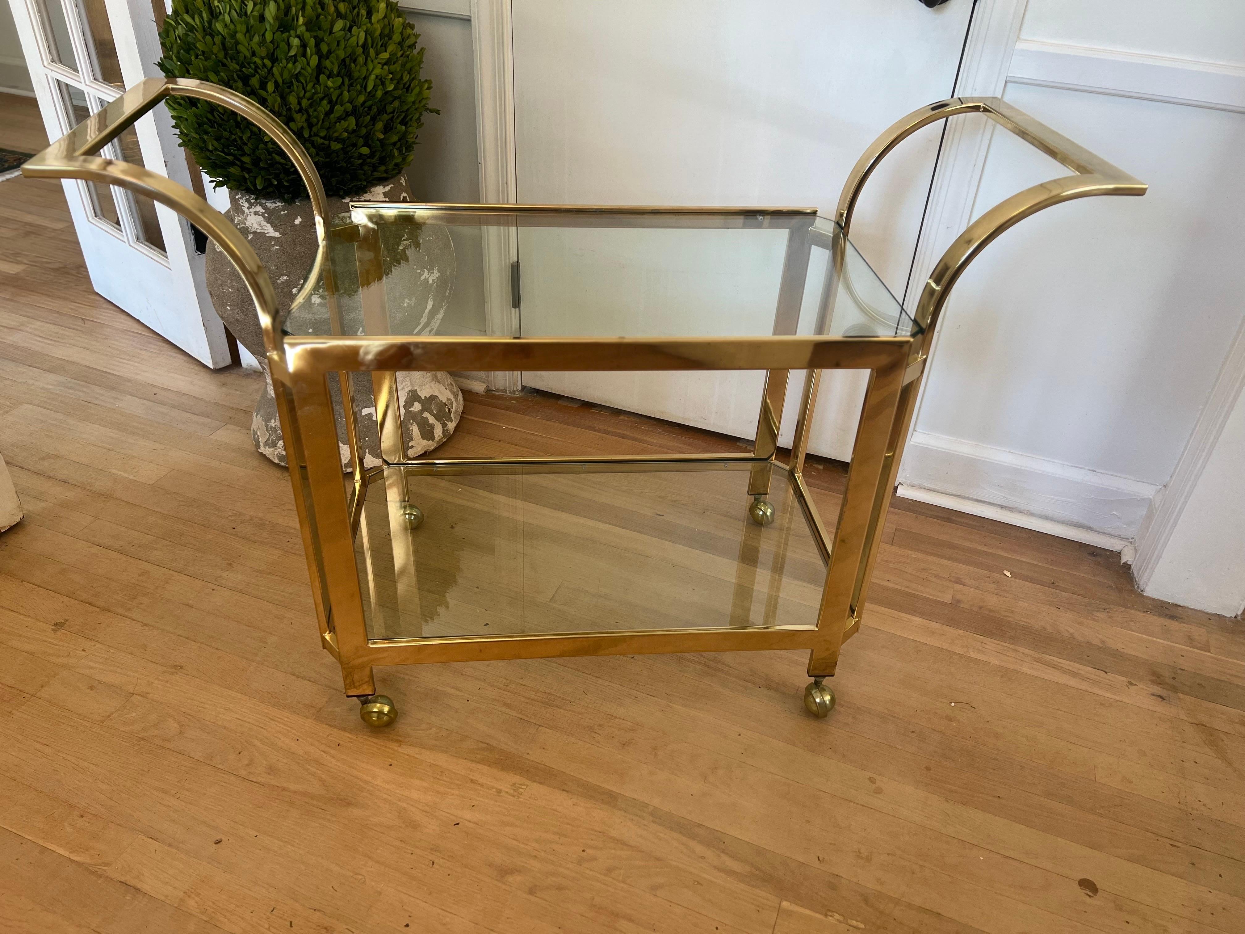 Mid Century Modern/MCM Two Tier Glass Bar Cart.  
Attributed to Milo Baughman/Thayer Coggin with flat bar curved brass contemporary/modern  design.
Four brass wheels that all roll smoothly. 

