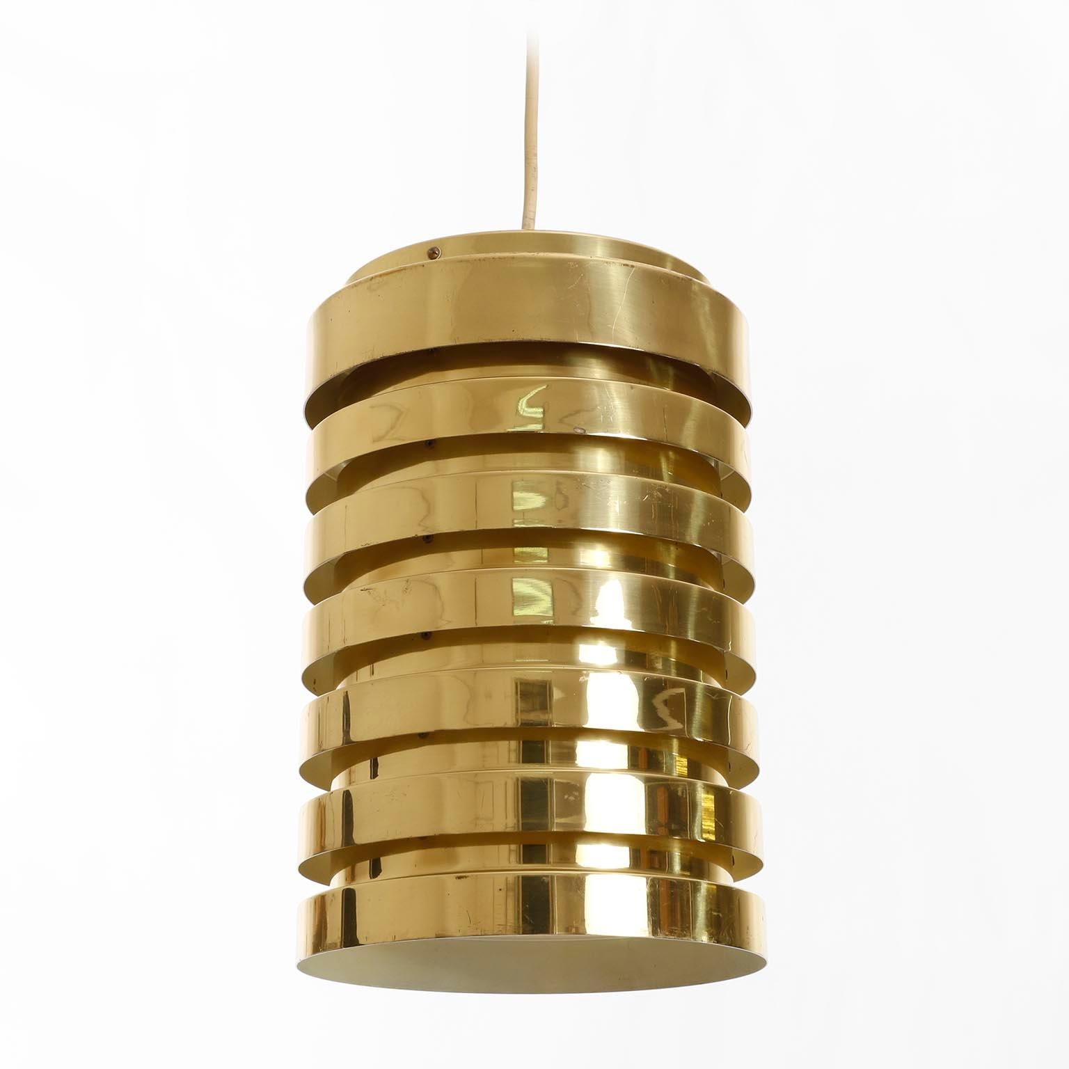 Lampe suspendue cylindrique en laiton massif poli, de style moderne du milieu du siècle, très bien patinée, conçue par Hans-Agne Agnes et fabriquée par AB Design/One Design-Light vers 1960.
L'intérieur est peint en blanc, vieilli et donc un peu