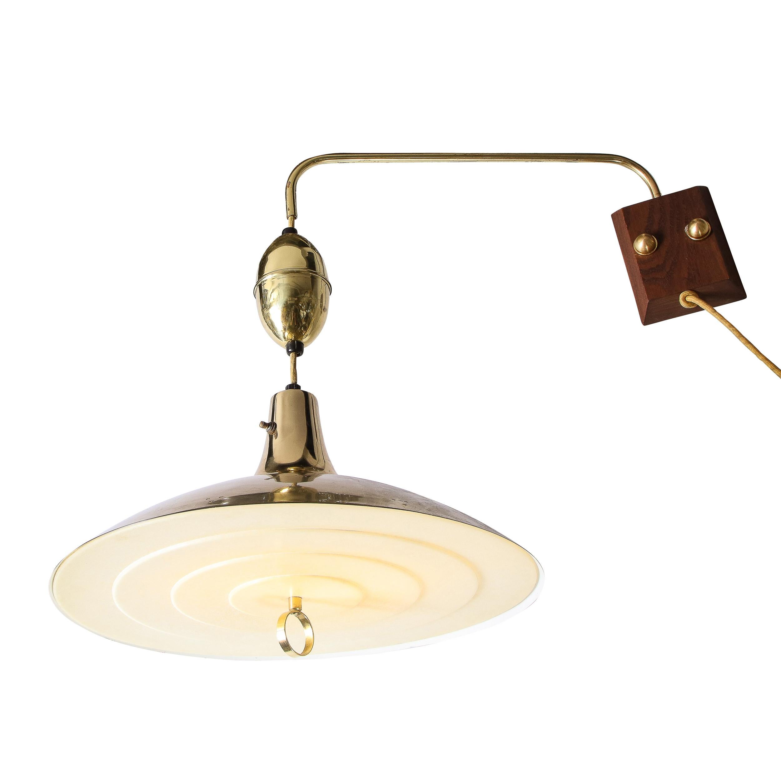 This stunning Mid Century Modern wall light , circa 1960 , features a sculptural polished brass concave body pierced with sets of three perforations (arranged in a pyramidal configuration with a tiered perspex shade concealing the shades fitted with