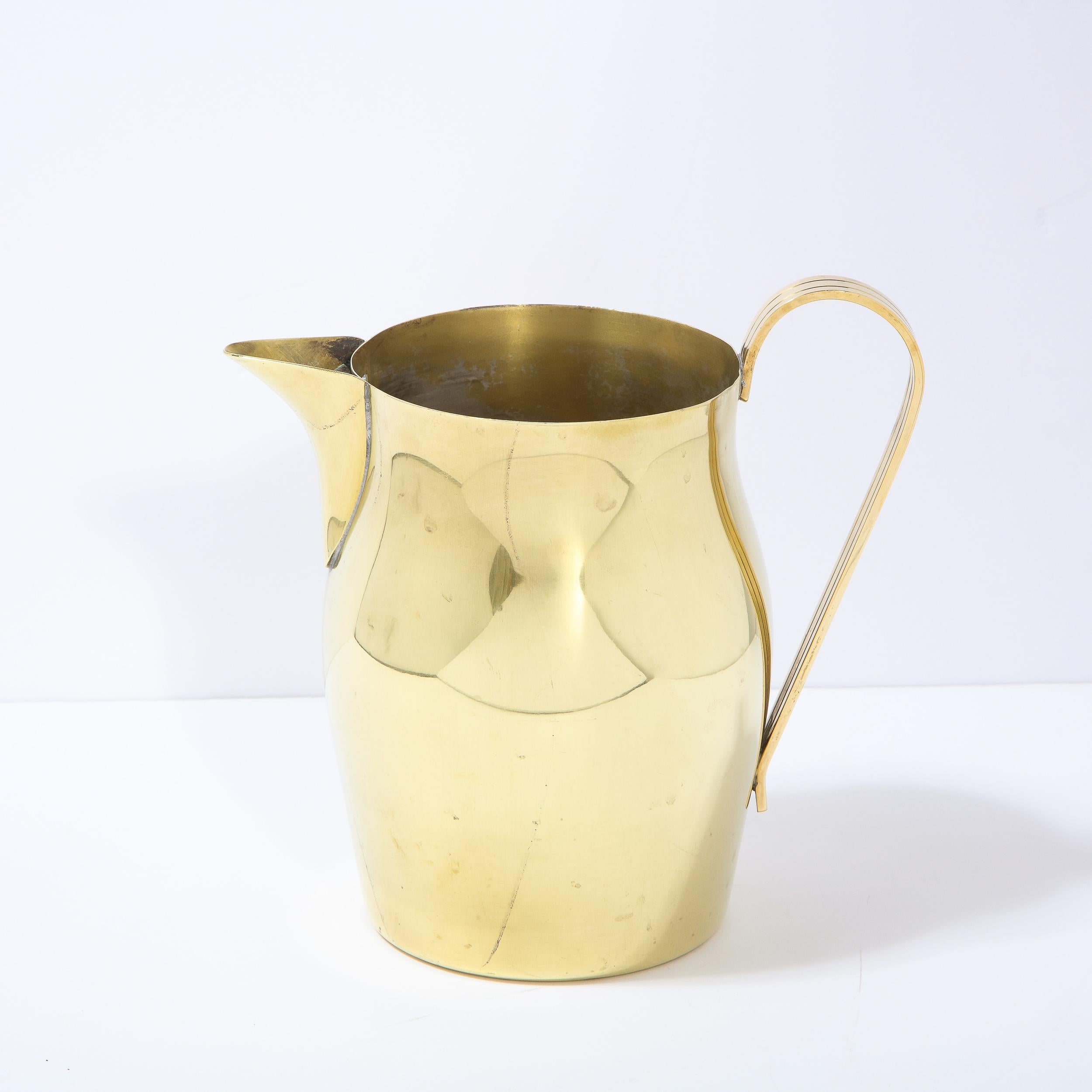 This elegant Mid-Century Modern polished brass pitcher was designed by Tommi Parzinger for Dorlyn Silversmiths in the United States circa 1960. It features an undulating body with a triangular concave beak-like spout and a curved and striated handle