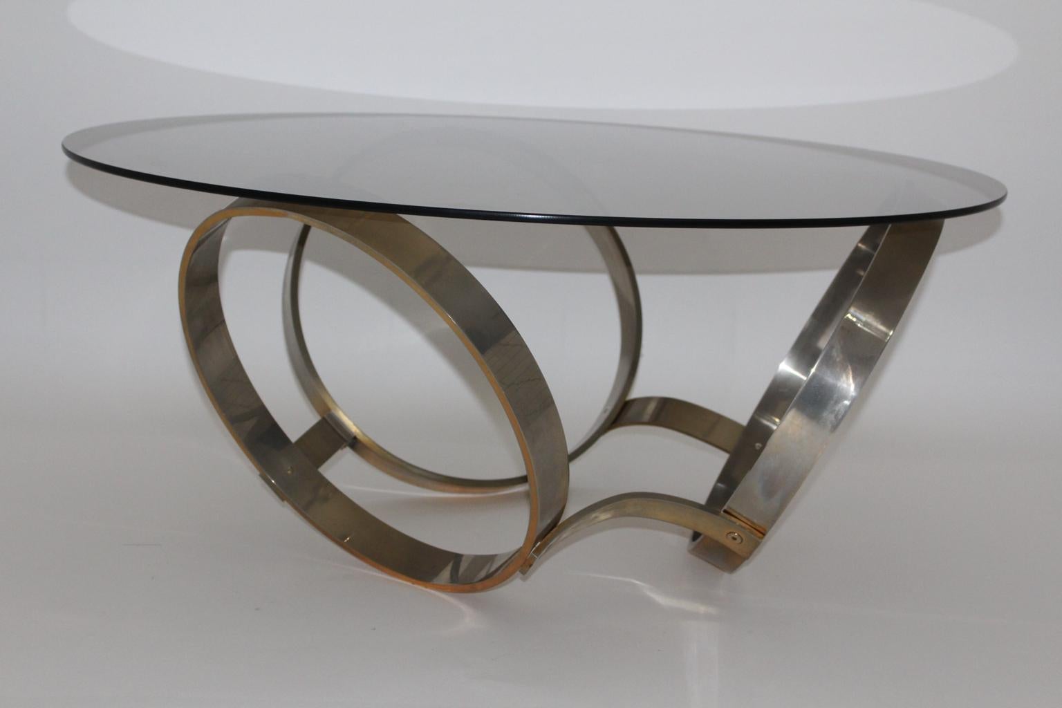 Space Age vintage coffee table or sofa table from brass plated metal and smoked glass plate circa 1970.
The brass plated metal base features three ring like elements as trinity.
Through the years and ages the brass plated metal base blends with