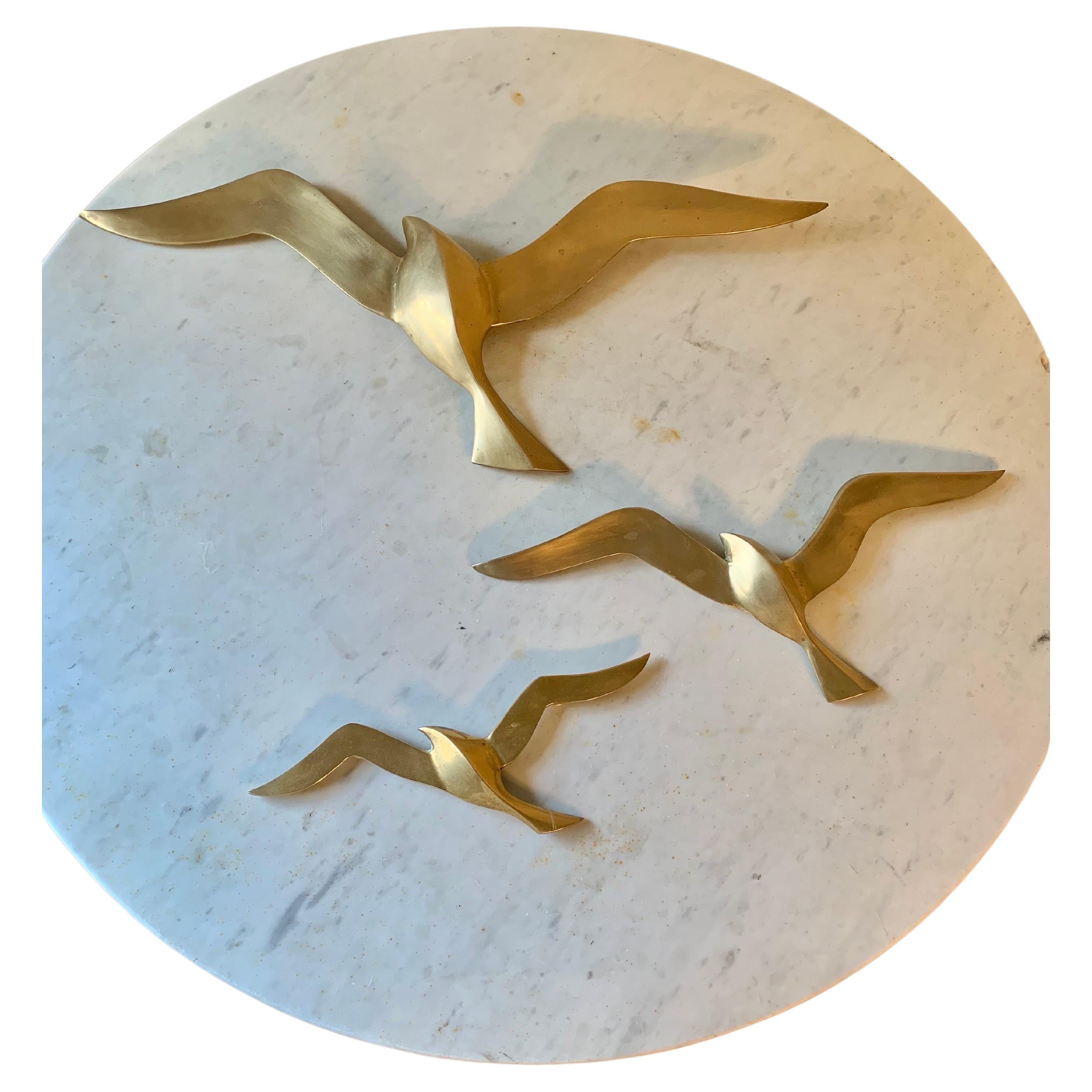 This iconic set of three wall sculptures depicts flying seagulls that were crafted from brass in the 1970's. Each bird graduates in size to exhibit a flock in flight and creates a work of wall art. Brass ring mounts are attached to the back of each