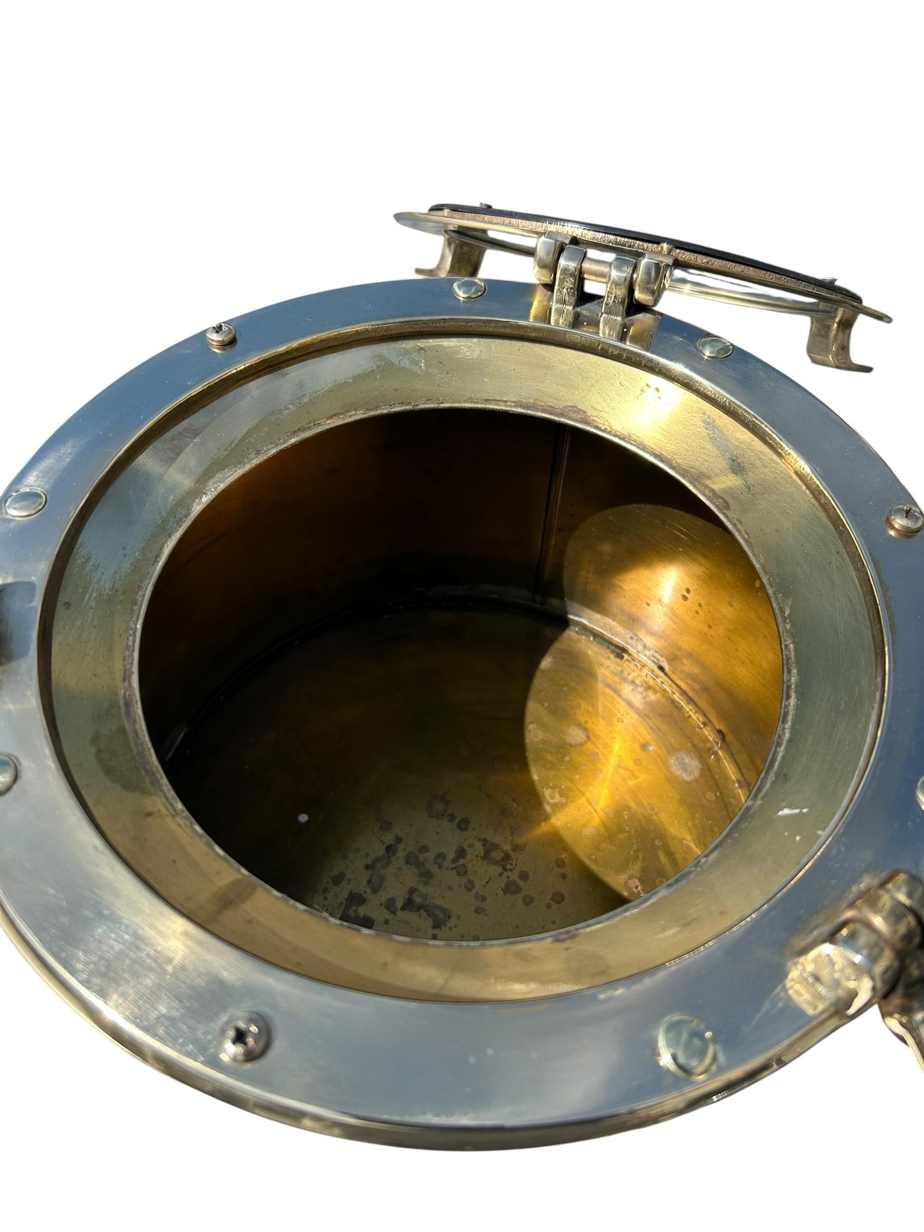 Cubitera vintage de latón de mediados de siglo, de forma cilíndrica, con tapa abatible de ojo de buey de barco, ventanilla de cristal y cierres de rosca que encierran un forro de zinc desmontable. Recién pulido.