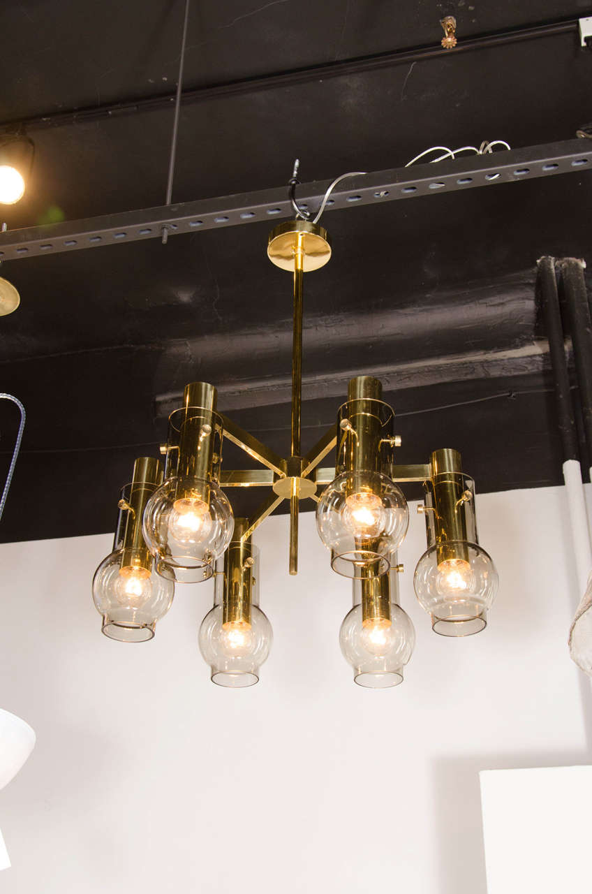 Ce lustre raffiné de style moderniste du milieu du siècle a été conçu par l'estimé Hans Agne Jakobsson en Suède, vers 1960. Il comporte six bras rectangulaires émanant d'un corps circulaire, le tout en laiton poli. Une tige cylindrique du même