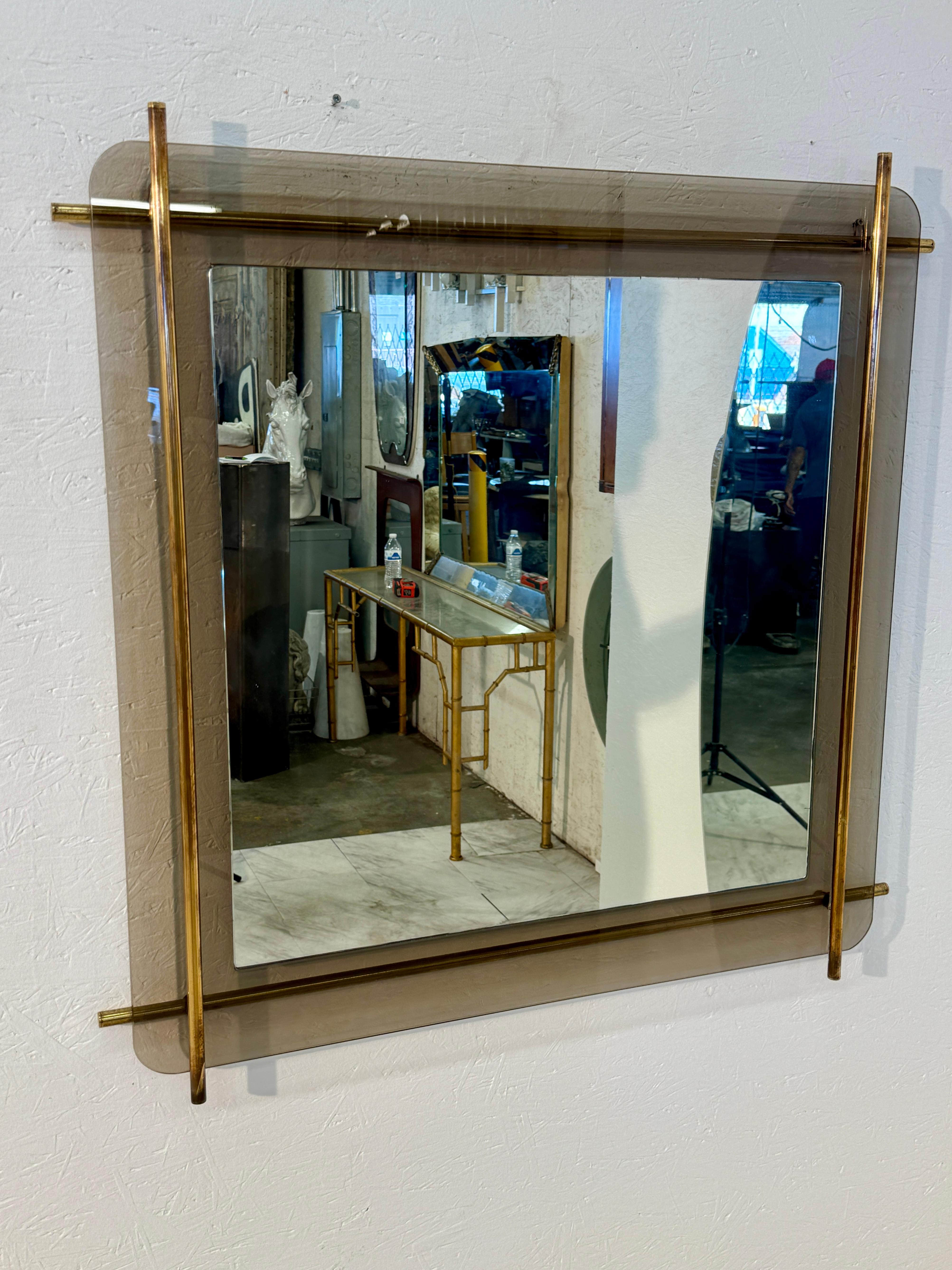Ein auffälliger, moderner Wandspiegel aus der Mitte des Jahrhunderts mit einem Rahmen aus Rauchglas, der von Messingrohrstäben eingerahmt wird, die über die Ränder hinausragen und einen kühnen, architektonischen Look erzeugen. Der Spiegel ist auf