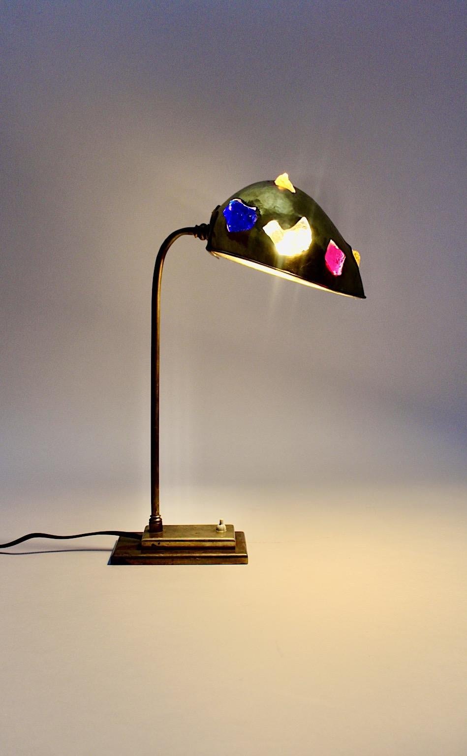 Mid-Century Modern vintage table lamp from brass and various multicolored unpolished glass stones Austria 1950s.
While the outstanding table lamp shows beautifully hammered brass shade with various multicolored glass stones, the downer part