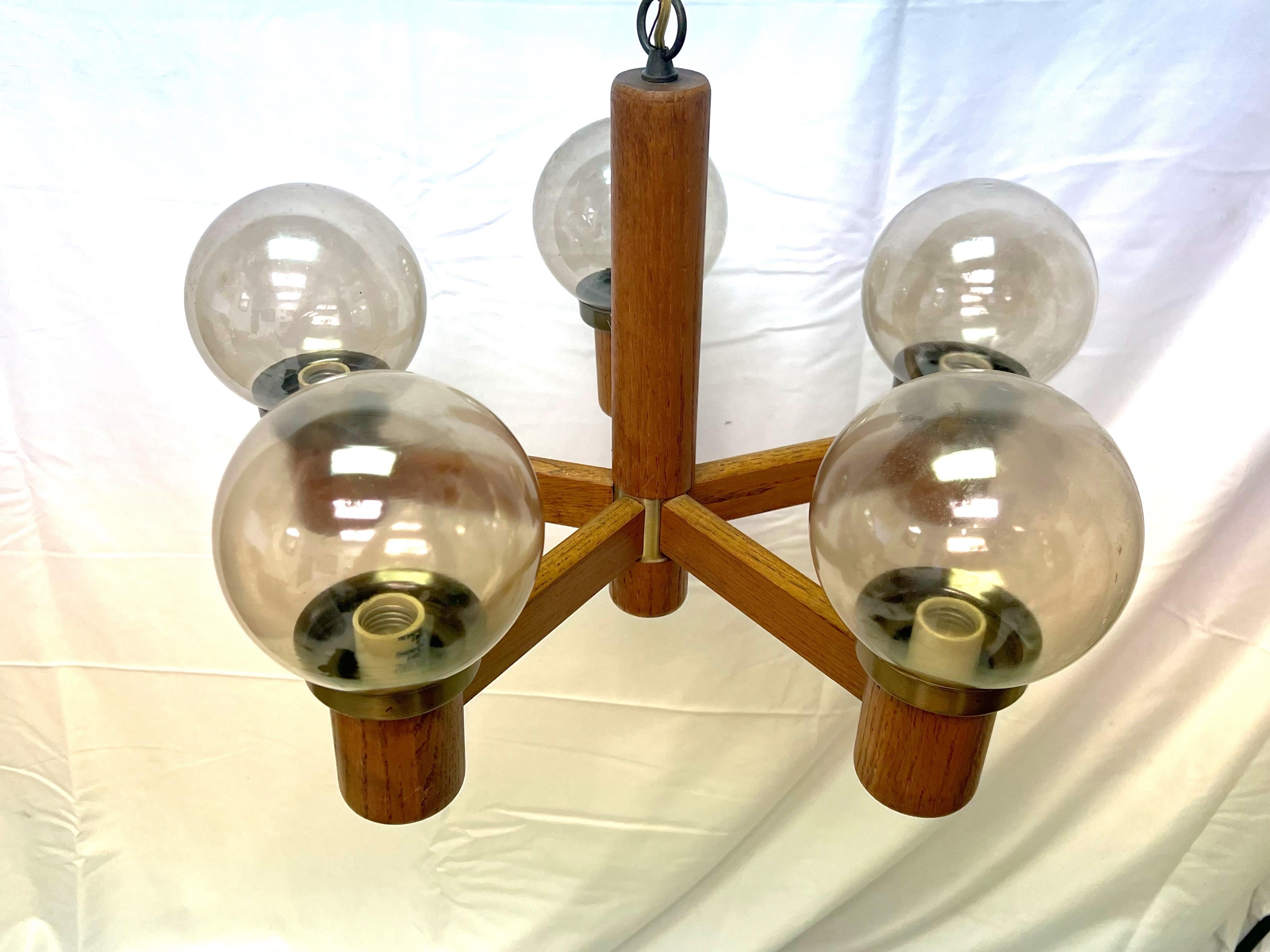 A gorgeous teak and brass 5 light chandelier with a brass canopy in a Danish style.   The smoked glass globes sit inside of the top of each bulb.   This piece is in its original condition and I suggest rewiring it… but it was working when removed