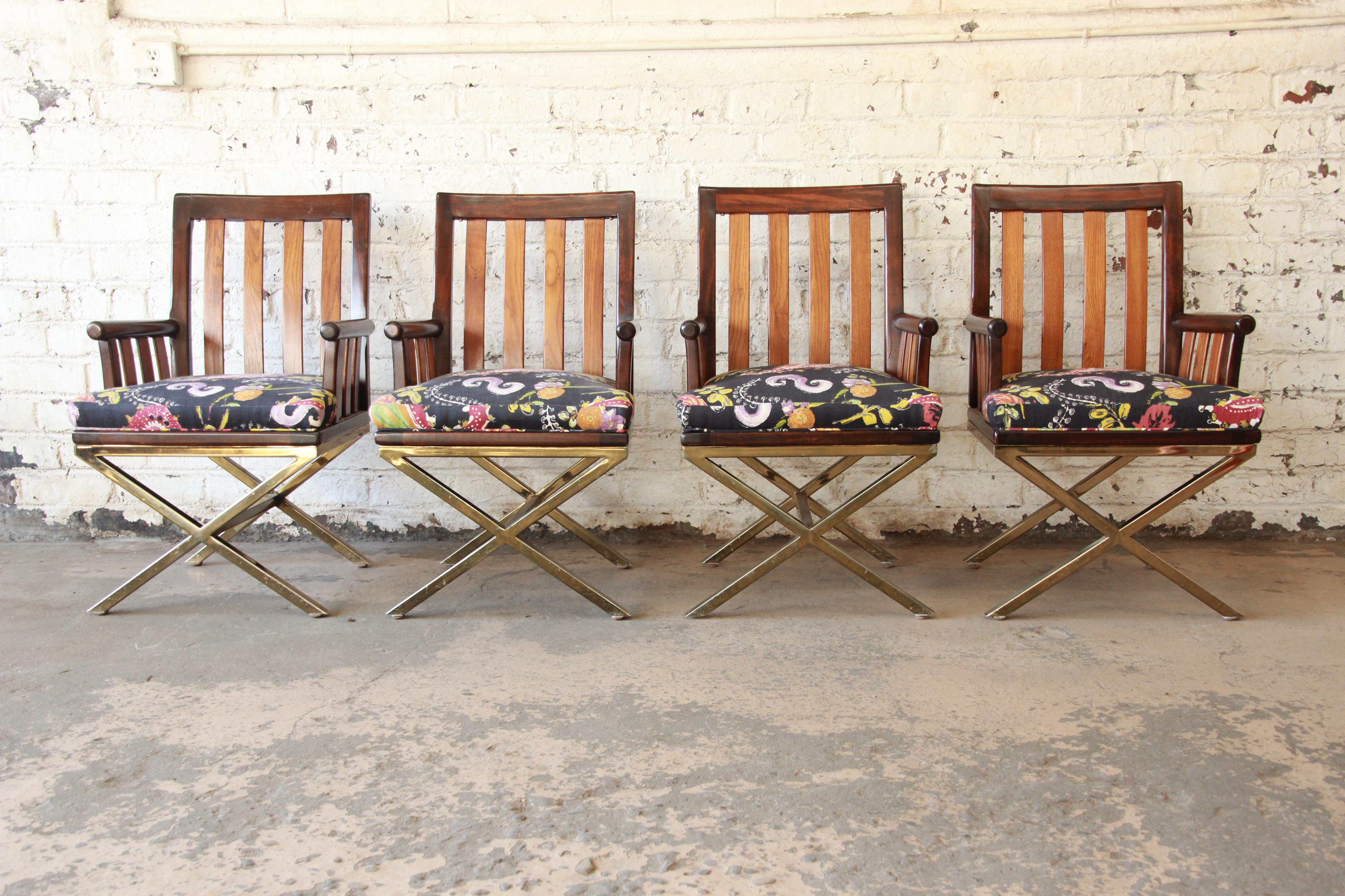 A unique set of four Mid-Century Modern armchairs. The chairs feature solid wood slatted backs and arms and a heavy brass X-base design. They have a colorful paisley upholstery which is clean and usable as is but could also easily be reupholstered.