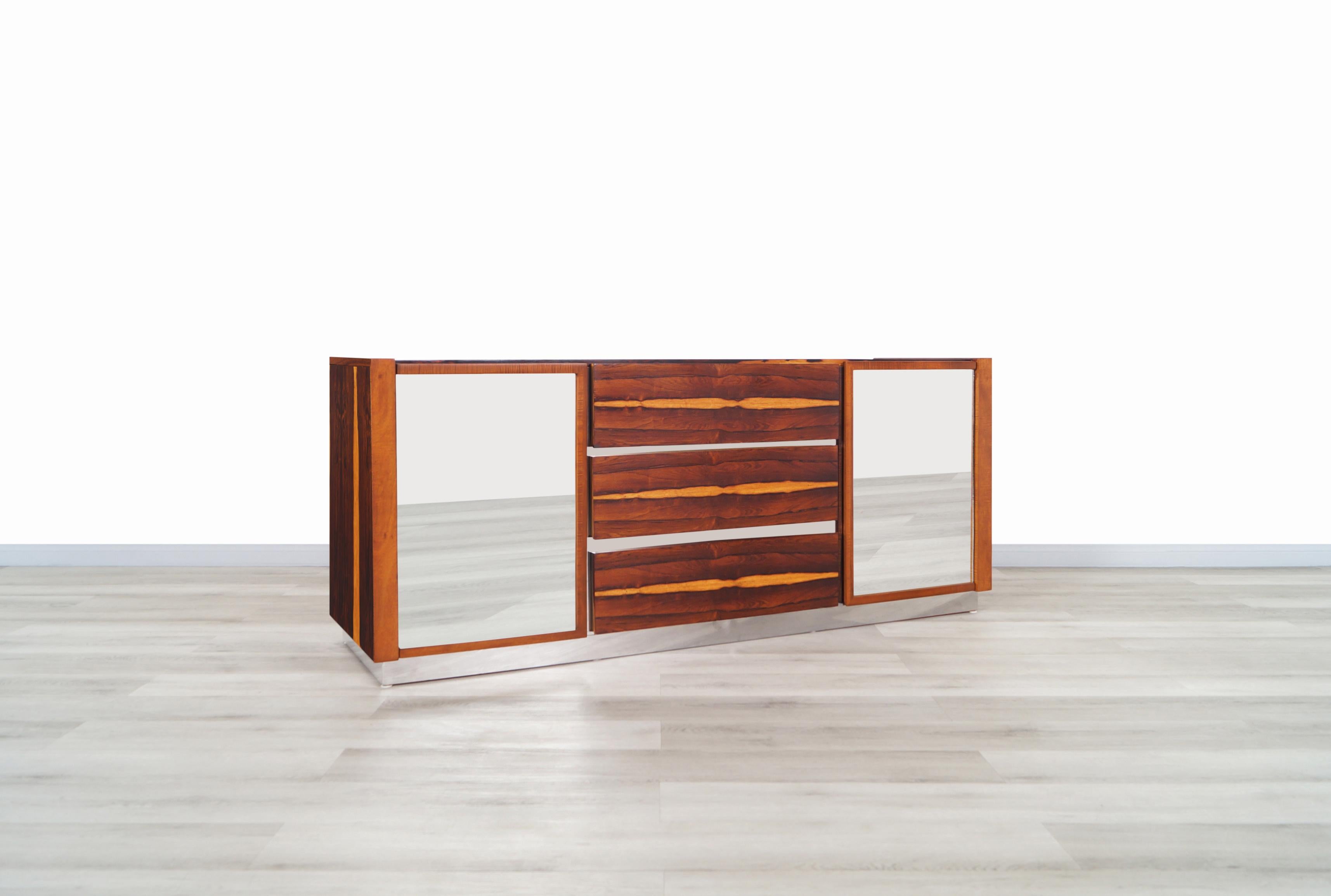 Mid-Century Modern rosewood credenza or dresser manufactured in the United States, circa 1960s. This credenza features a total of nine drawers. Three drawers are hidden behind each mirrored glass door. Plenty of storage space. The case consists of a