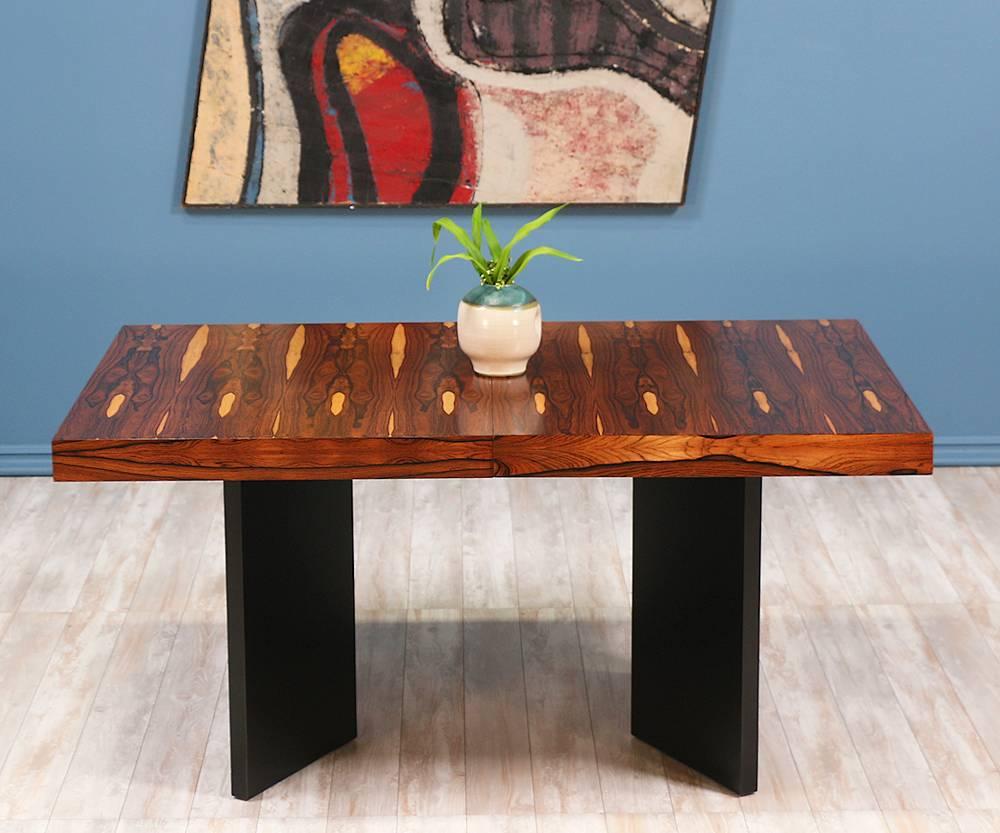 Mid-Century Modern dining table designed and manufactured in the United States circa 1960’s. This extraordinary dining table includes two removable extension leaves that provide extra length when desired. The elaborate Brazilian rosewood grain shows