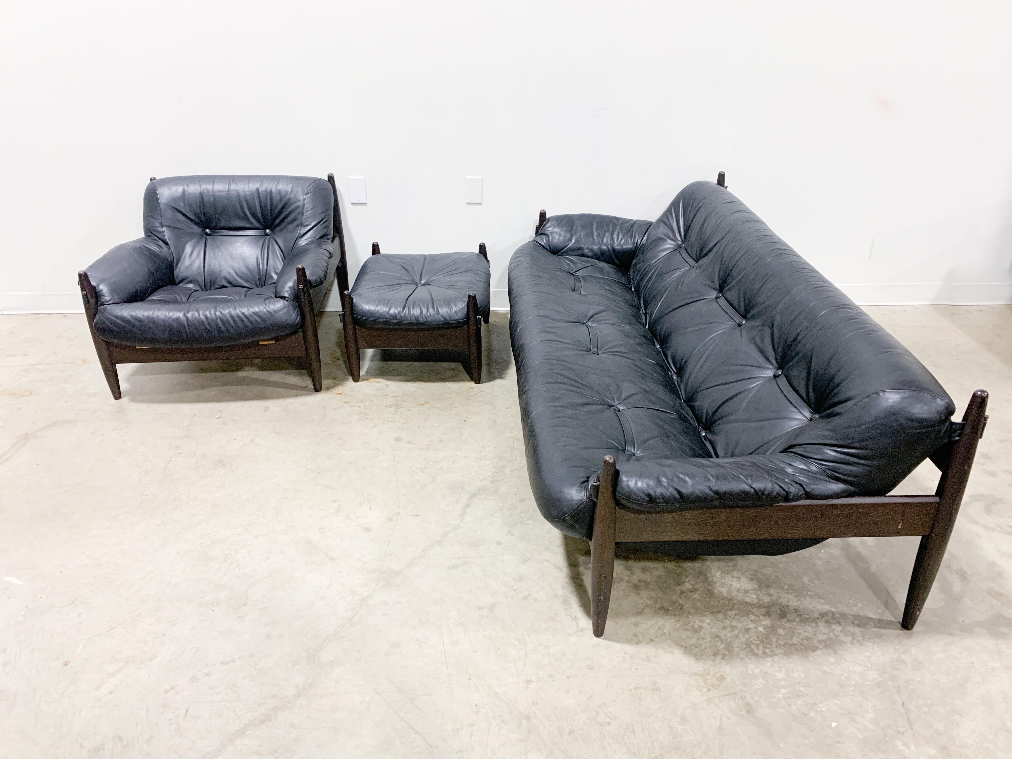 Strikingly beautiful Brazilian modernism style set with ebonized wood frames and genuine leather sling seats in the style of Sergio Rodrigues. Set is in excellent original condition and includes a three-seat sofa, lounge chair, ottoman and slate top