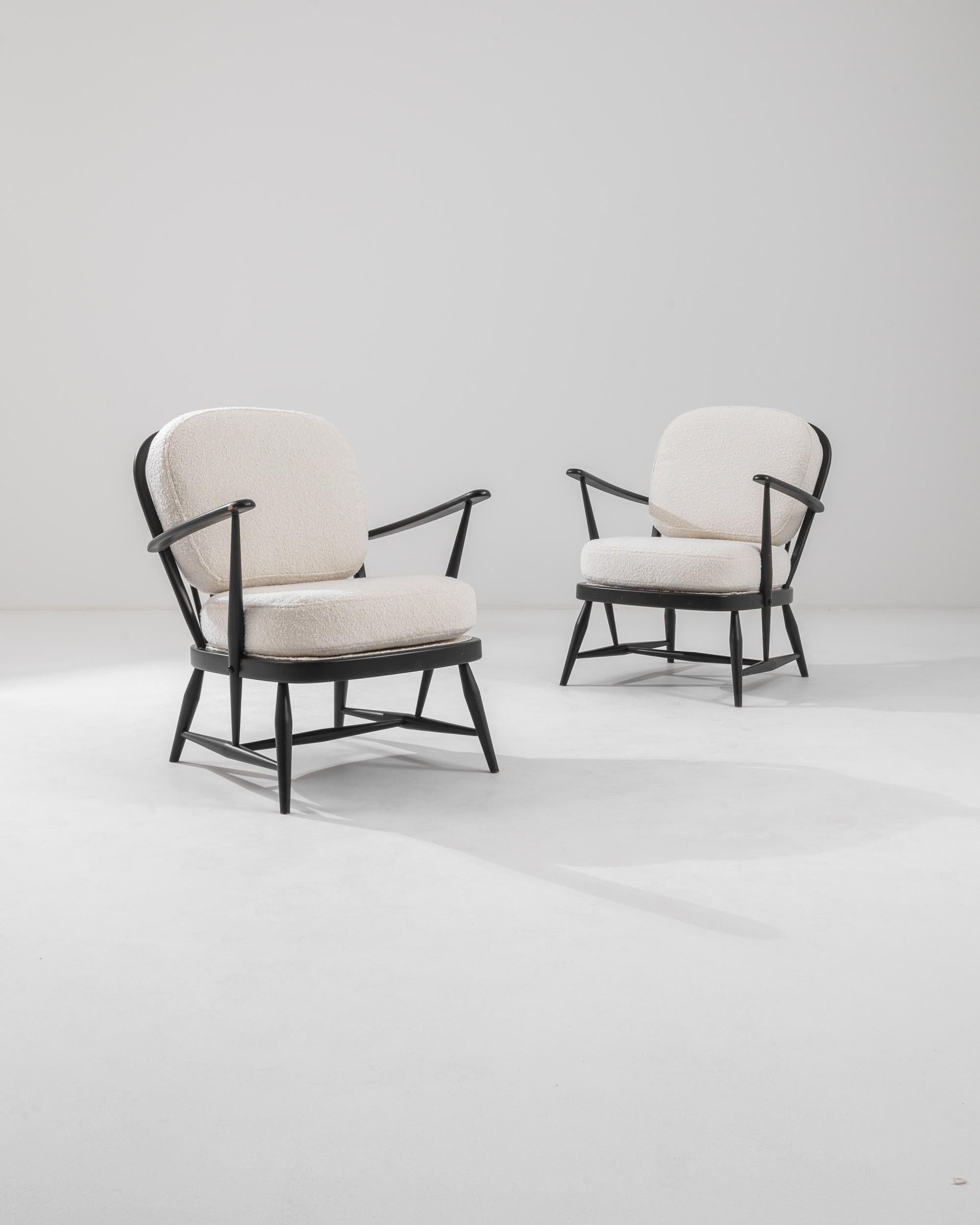 This stylish pair of vintage armchairs combine homey farmhouse elements with a bold Modernist approach. Made in the United Kingdom in the 20th century, slender spindles, typical of traditional Windsor chairs, are arranged into a novel silhouette.