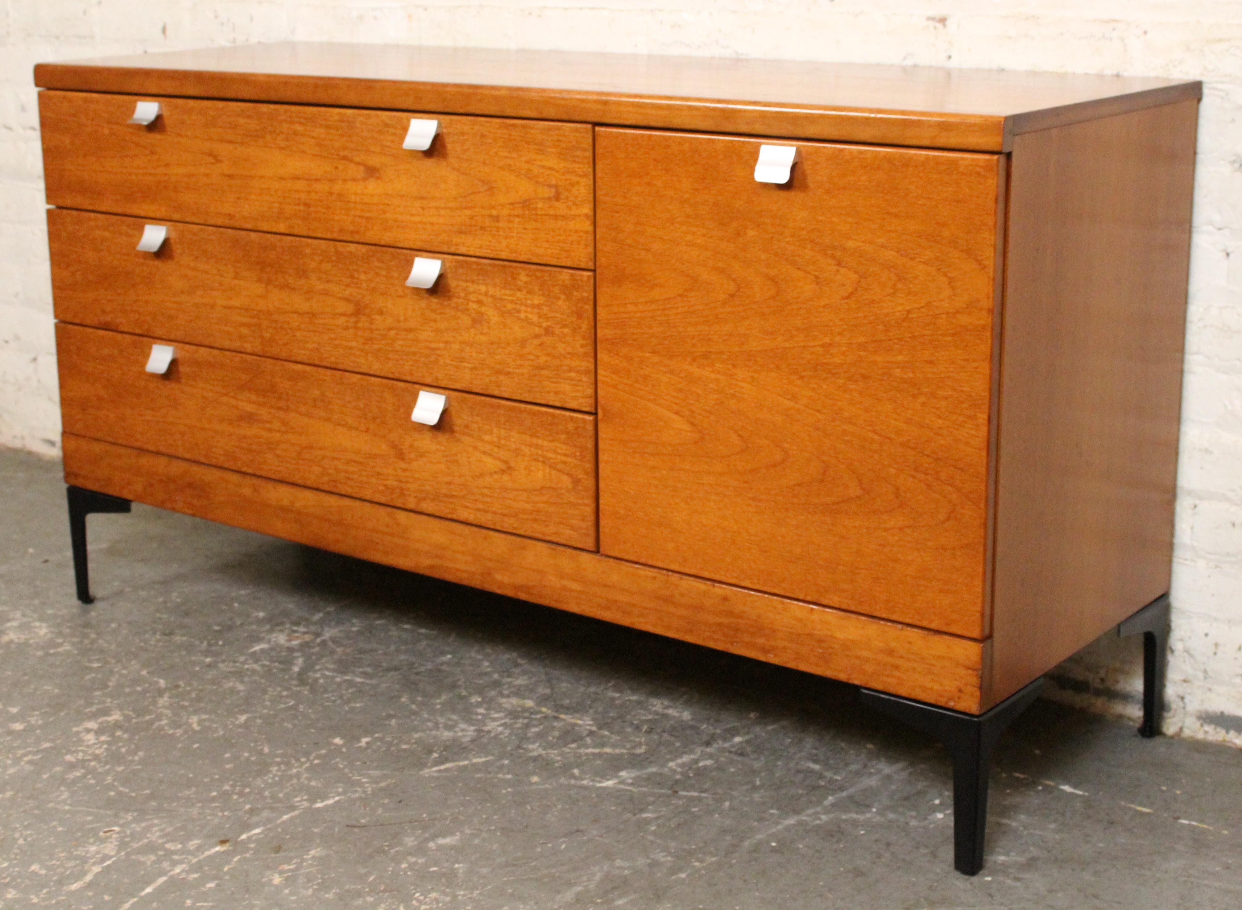 A striking example of British Mid-Century design, this teak lowboy dresser by White & Newton features a sleek profile with three wide drawers and a single side door for versatile storage. Distinctive white aluminum handles and black aluminum legs