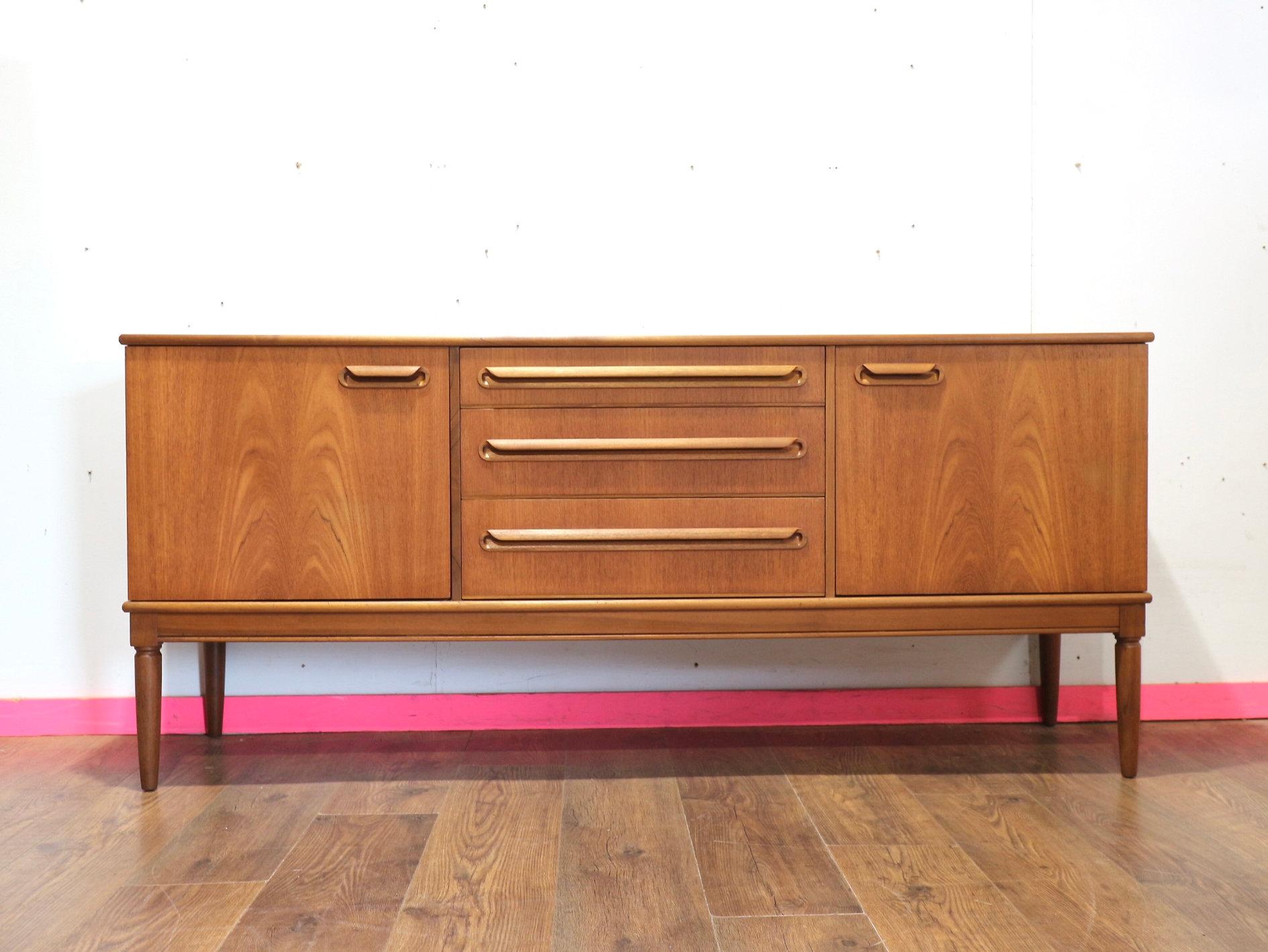 Discover the exquisite elegance of our Mid Century Modern British Vintage Teak Sideboard Credenza. This exceptional piece offers great storage, seamlessly blending functionality with style. Admire the beautifully turned legs and appreciate the