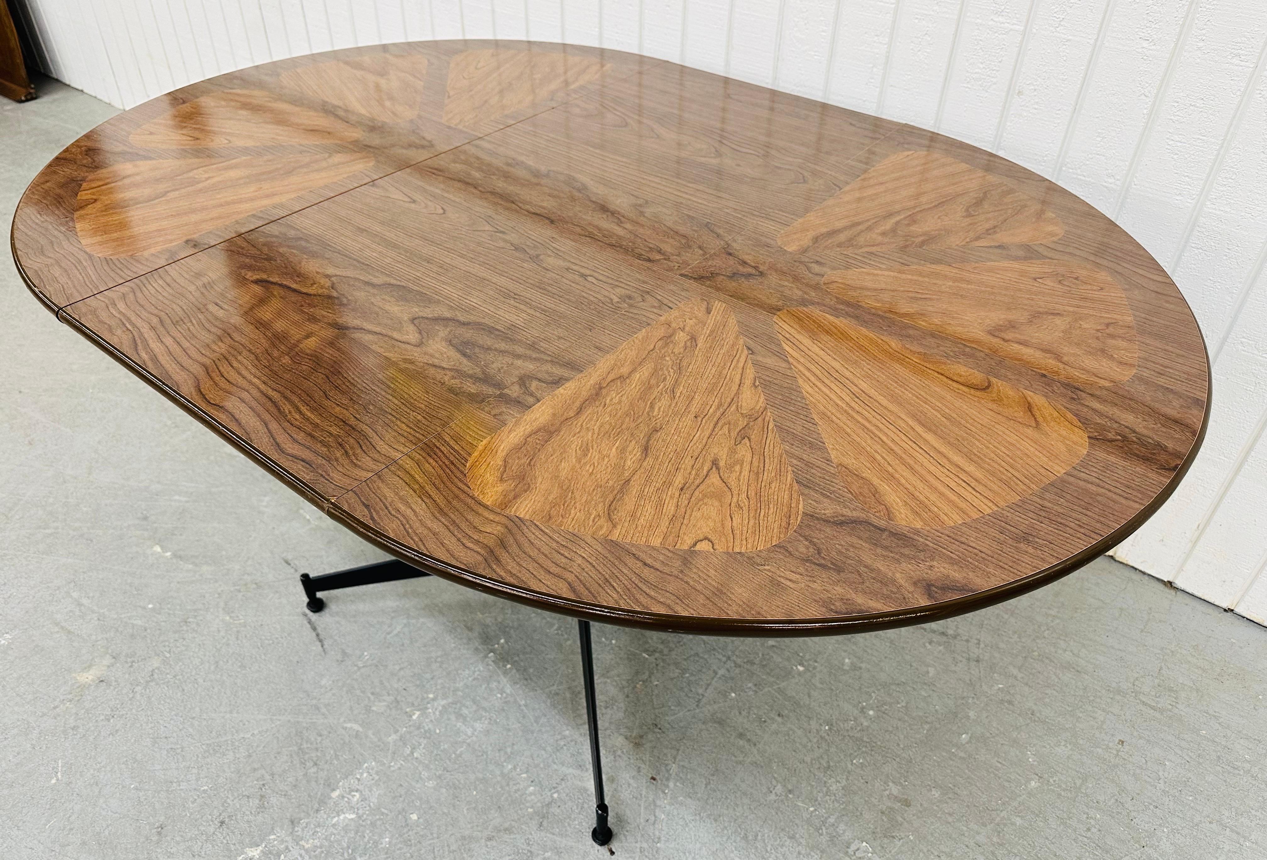 This listing is for a Mid-Century Modern Brody Walnut Dining Set. Featuring a laminated walnut round table that expands to 59” L with one leaf, black metal base, four swivel dining chairs with walnut backs, leather cushions, and black metal legs.