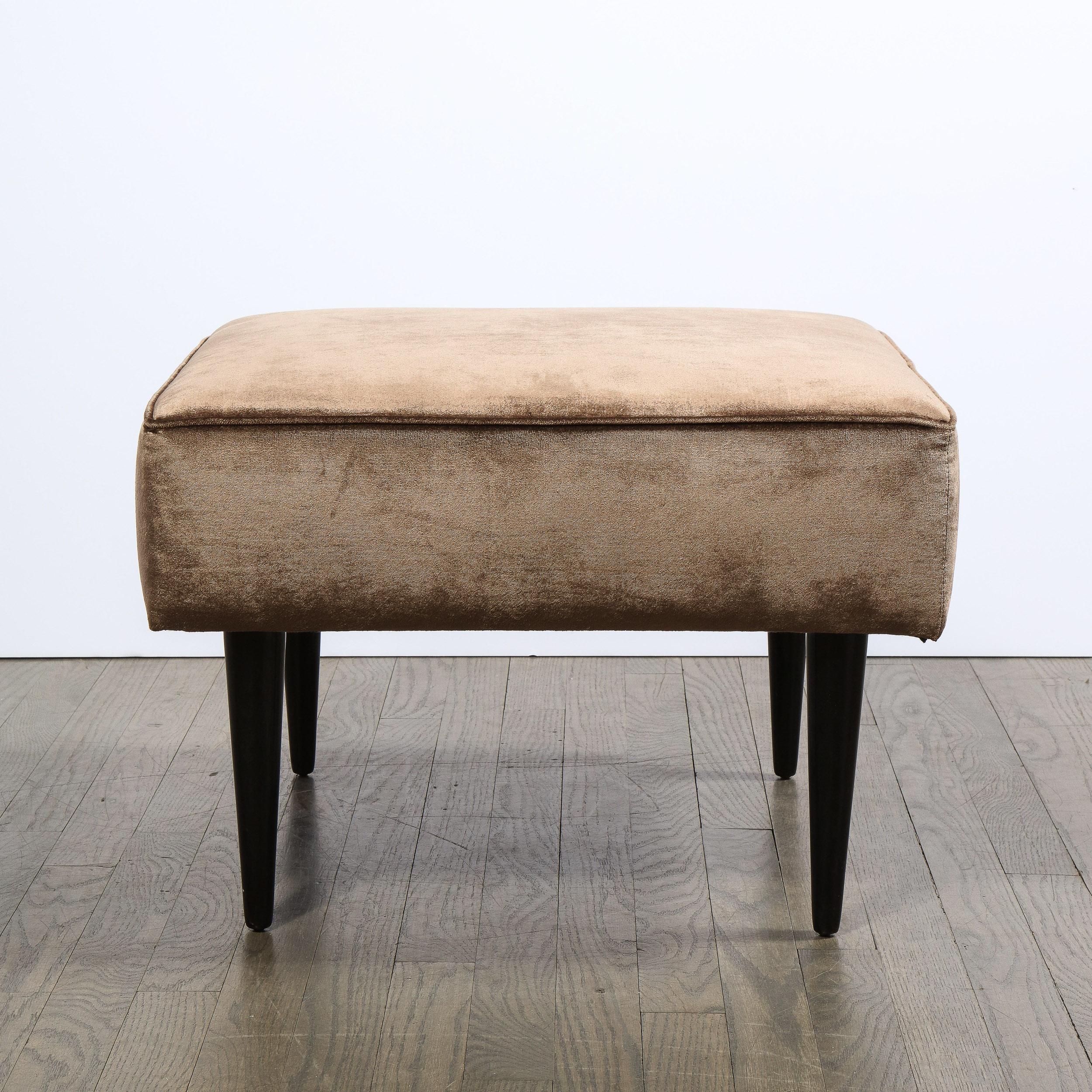 This elegant and sophisticated Mid-Century Modern ottoman was realized in the United States, circa 1960. It ottoman offers a rectangular form with piping detailing on the perimeter of the top and straight conical legs. The ottoman have been newly