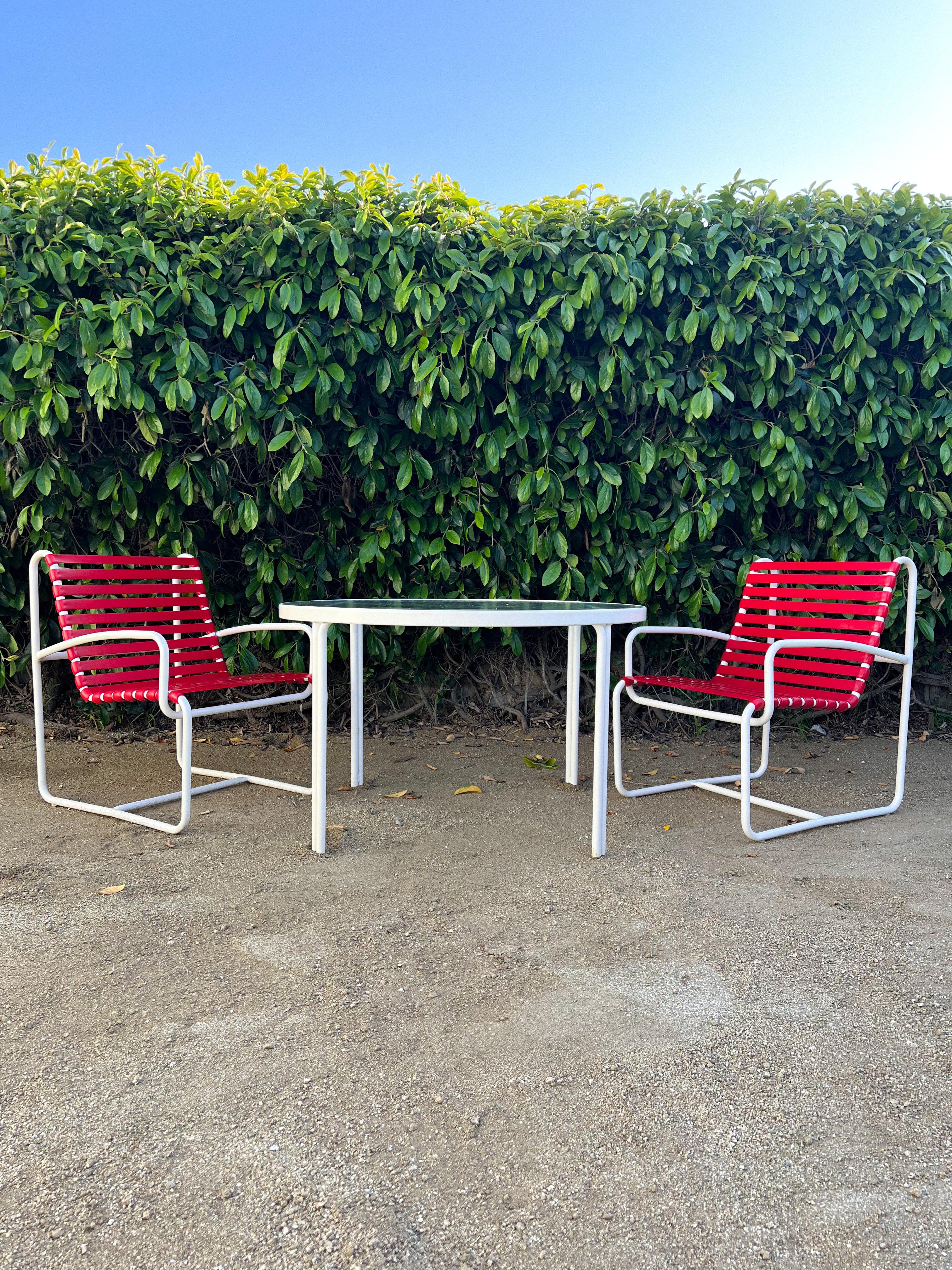 Outdoor 3-piece dining set with 2 chairs and dining table designed in the 1970s by Brown Jordan (unmarked). Original red vinyl straps on metal frames powder coated in white. 

The table features a textured glass in a very mid century style.

Table: