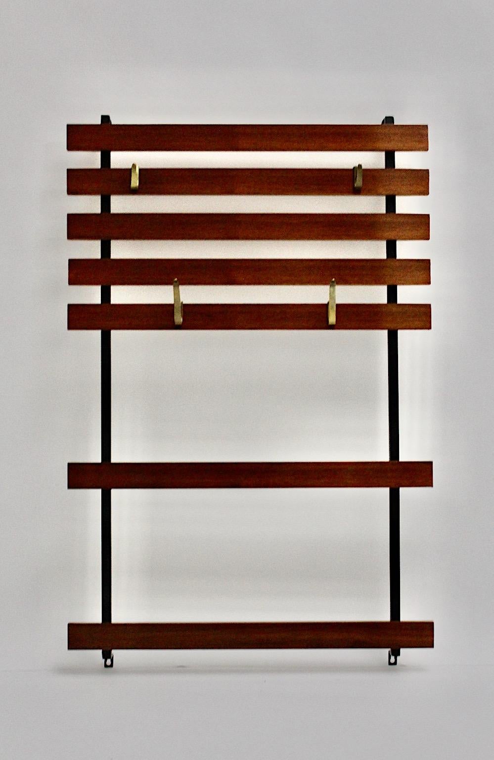 Mid Century Modern wall mounted coat rack from walnut in warm brown color and black lacquered metal with four original brass hooks by Carl Auböck 1950 Vienna.
Seven stained walnut slats are fixed at the black lacquered metal frame, while four solid