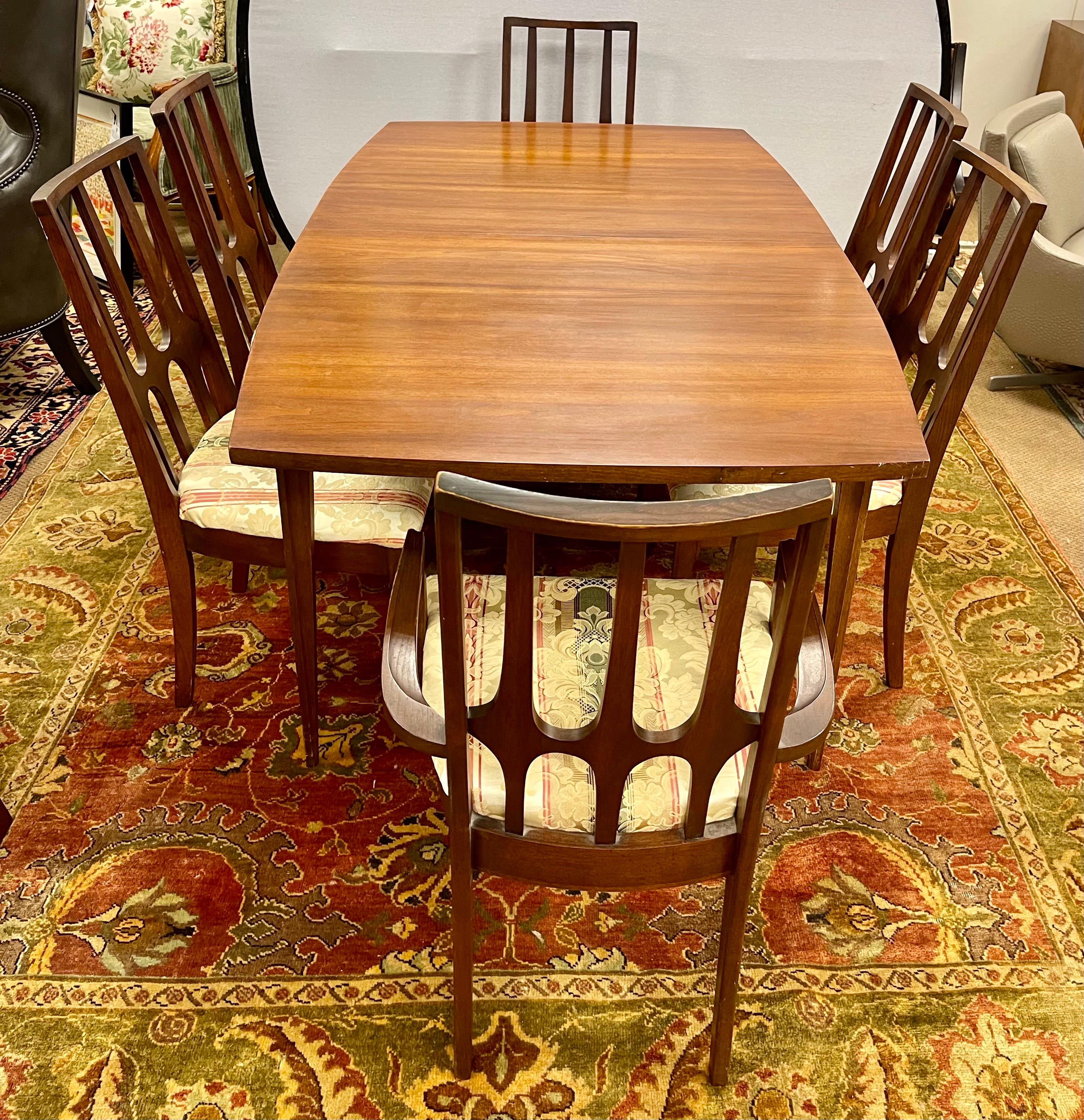 Iconic Broyhill walnut dining room table with rare and sought after boat shaped top that comes with six matching chairs. Circa 1962. There are four side chairs and two arm chairs. The table is expandable with one leaf that can expand the table by