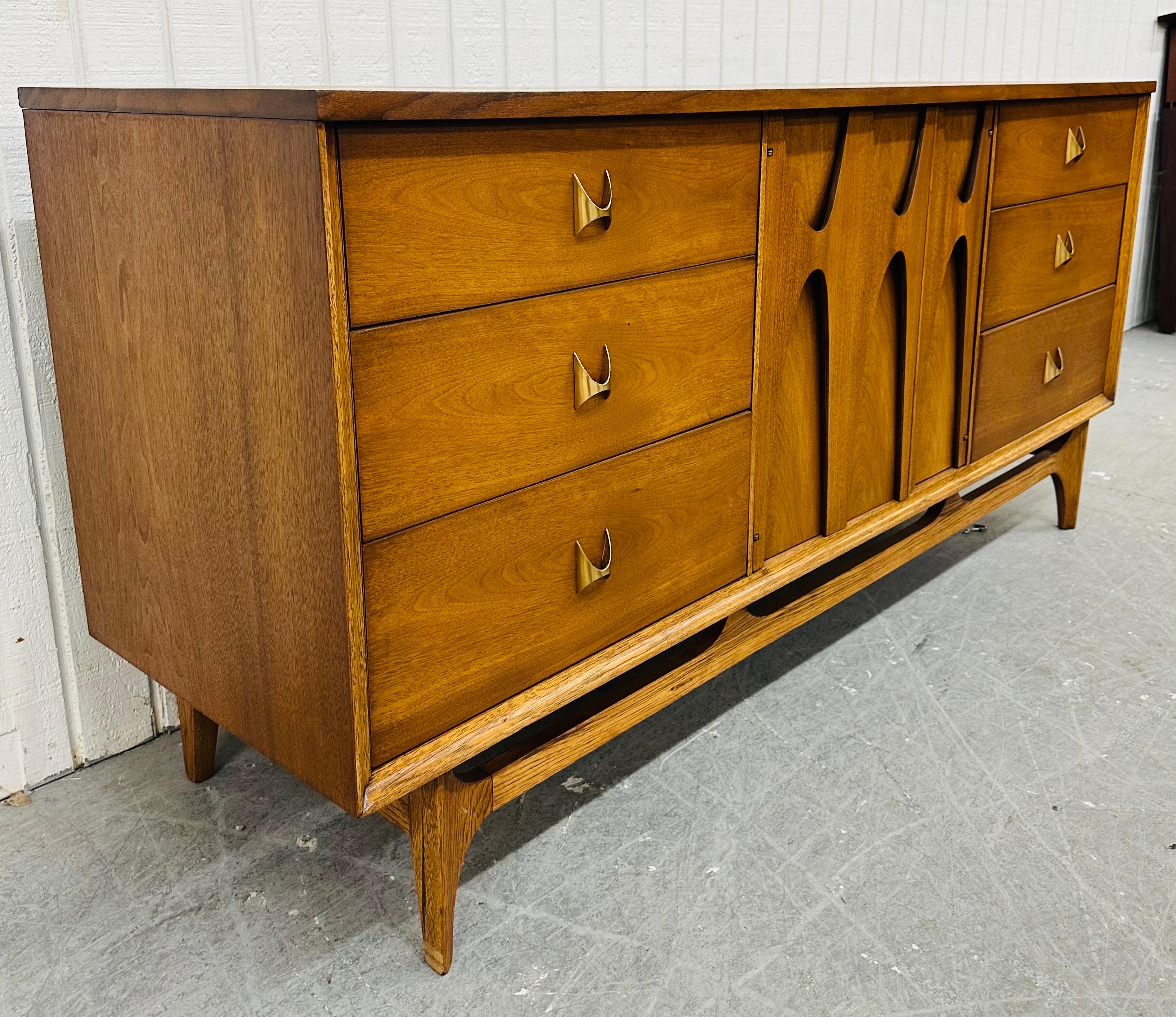 This listing is for a Mid-Century Modern Broyhill Brasilia Walnut 9-Drawer Dresser. Featuring a straight line design, three drawers on each side with original Brasilia brass hardware, sculpted center doors that open up to three hidden drawers,