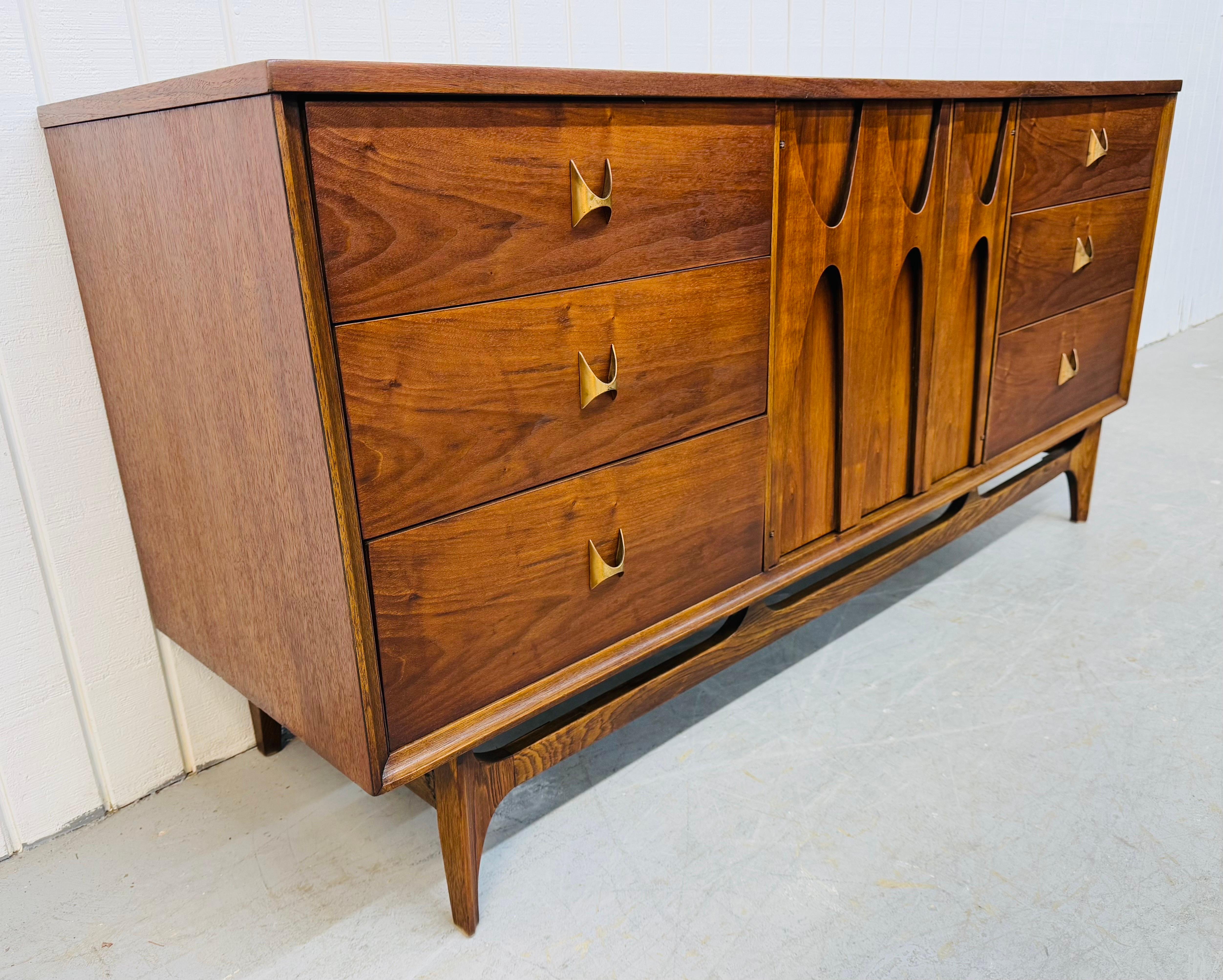 This listing is for a Mid-Century Modern Broyhill Brasilia Walnut 9-Drawer Dresser. Featuring a straight line design, three drawers on each end, sculpted center doors that open up to three hidden drawers, modern legs with stretcher base, original