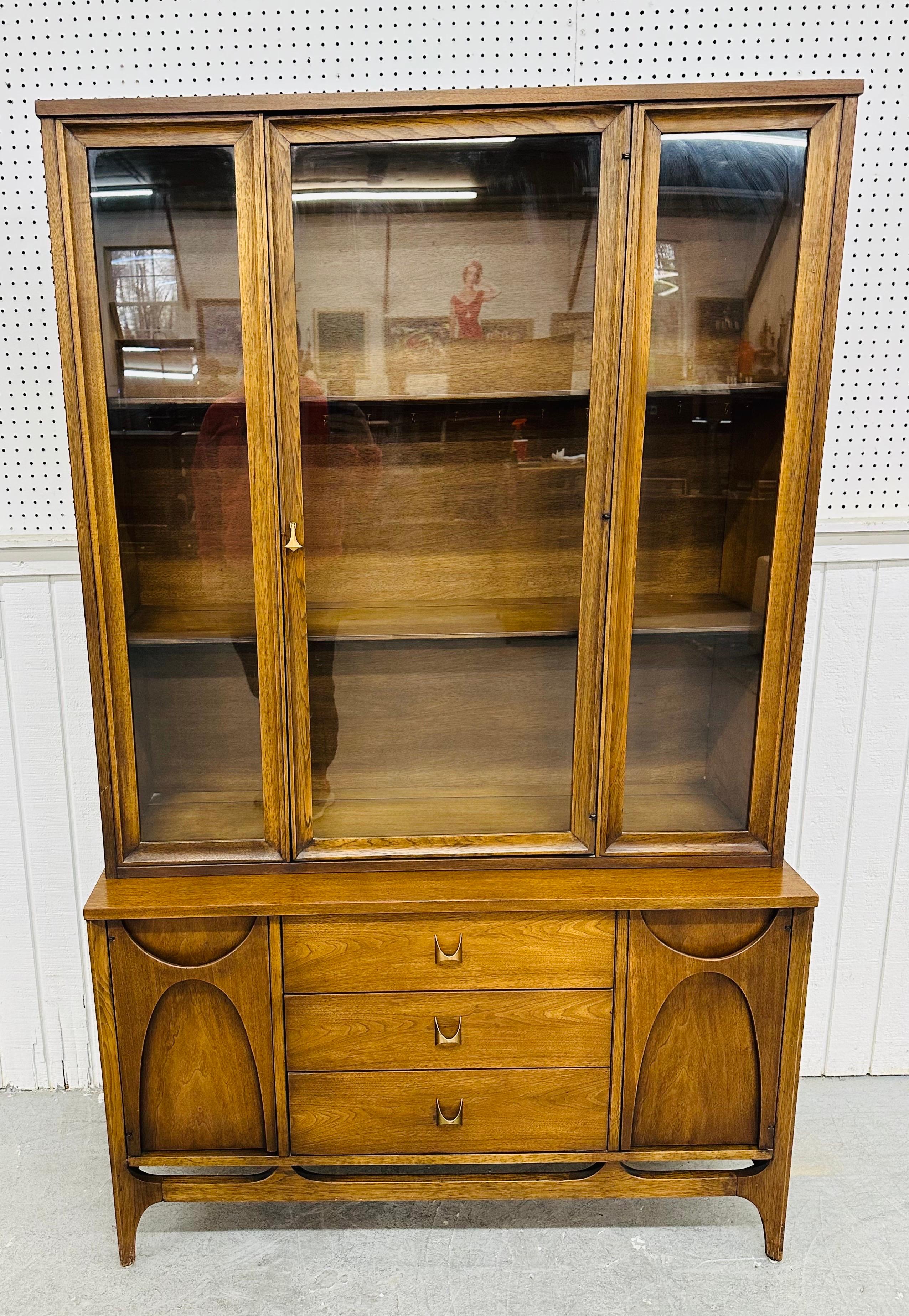This listing is for a Mid-Century Modern Broyhill Brasilia Walnut Display Cabinet. Featuring a straight line design, a removable top with center door that opens up to two fixed shelves, bottom cabinet with two sculpted doors that open up to storage