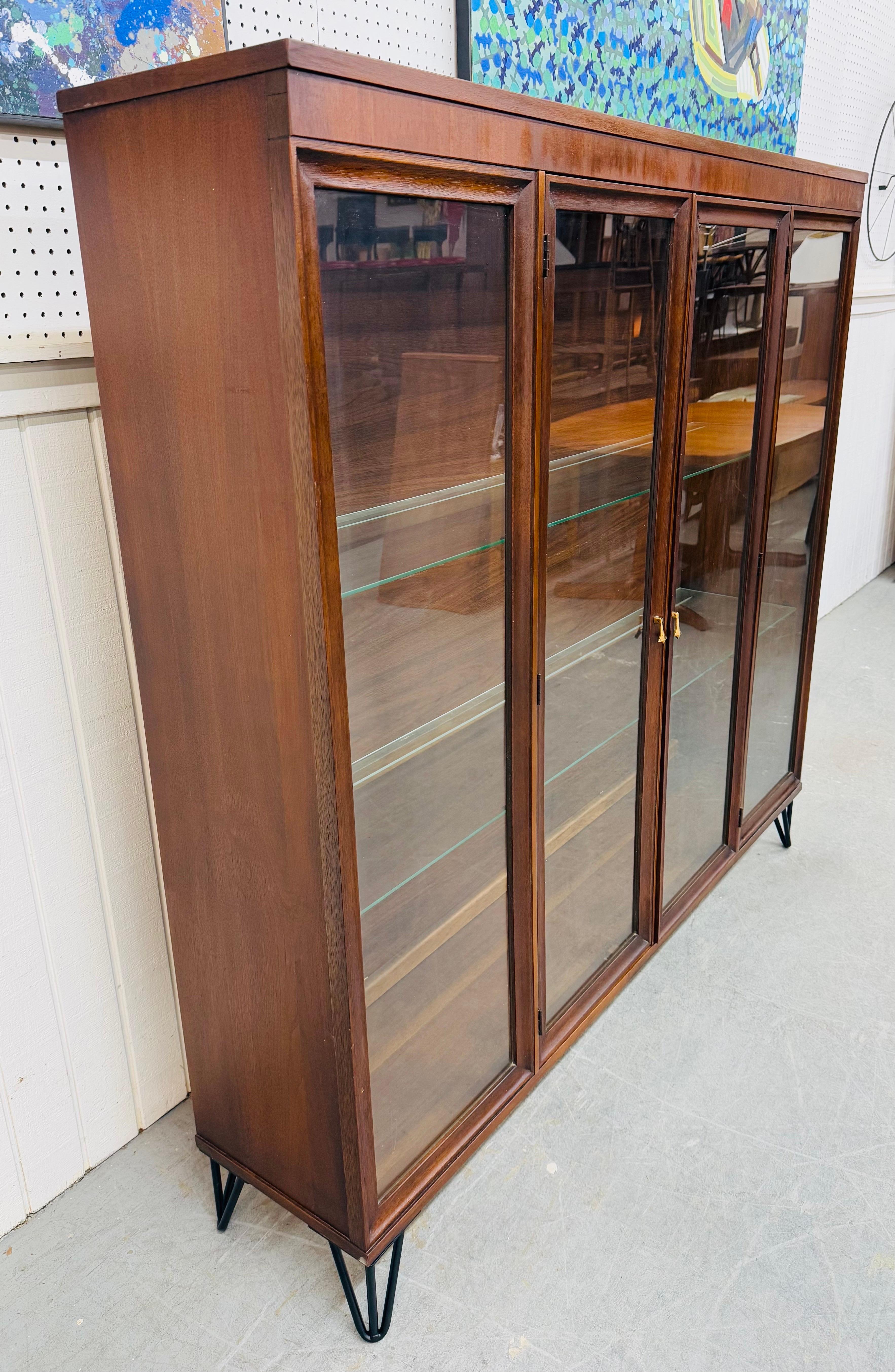 This listing is for a Mid-Century Modern Broyhill Brasilia Walnut Display Case. Featuring a straight line design, walnut cabinet with glass display front, two doors with original pulls that open up to glass shelves, and black metal hairpin legs.
