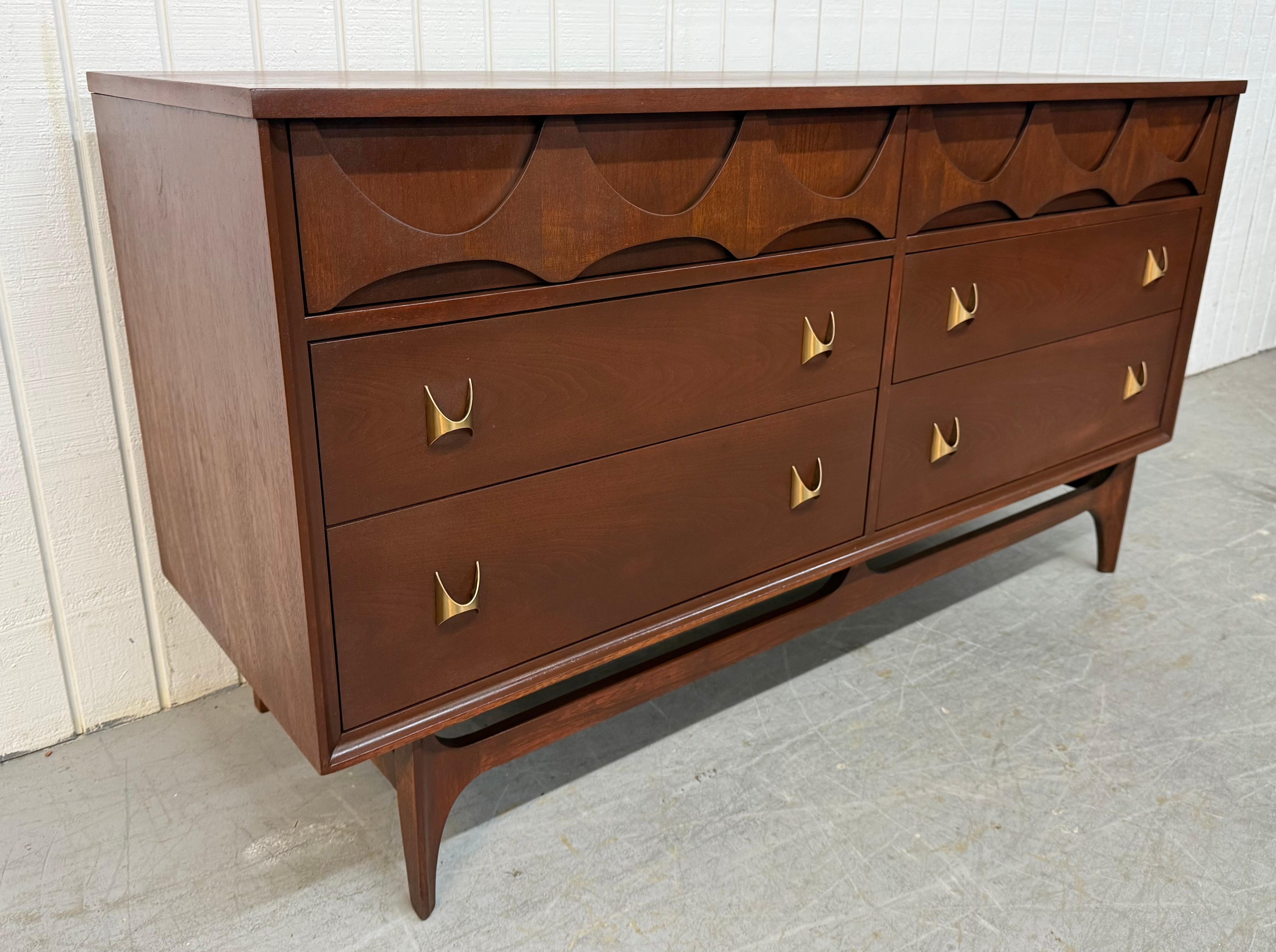 This listing is for a Mid-Century Modern Broyhill Brasilia Walnut Dresser. Featuring a straight line design, six drawers for storage, iconic sculpted Brasilia top drawer pulls, original brass hardware, modern legs with stretcher base, and a