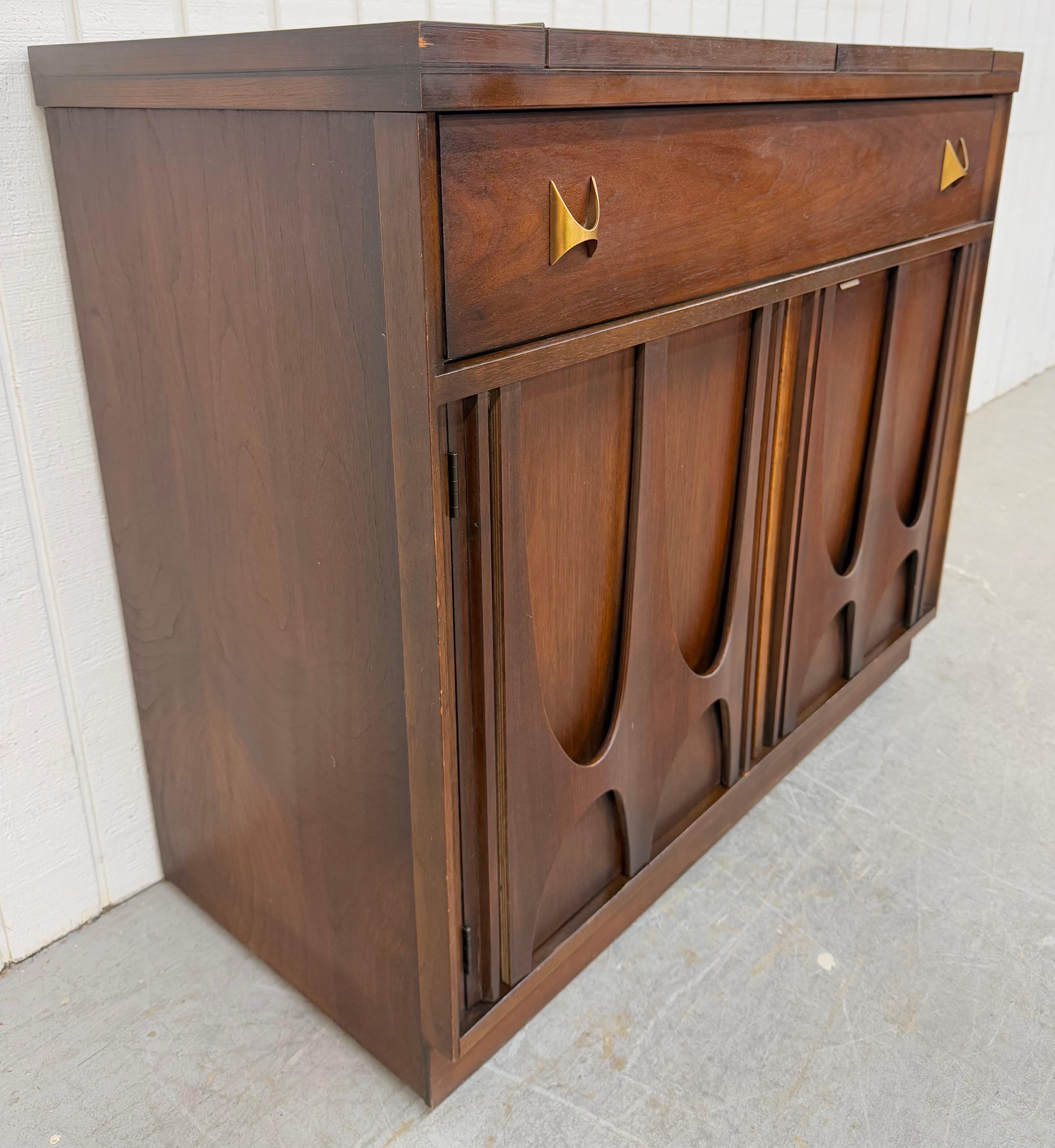This listing is for a Mid-Century Modern Broyhill Brasilia Walnut Flip-Top Server. Featuring a straight line design, laminated acid washed top that flips open to 59.5” L for serving, single drawer with original Brasilia brass hardware, sculpted